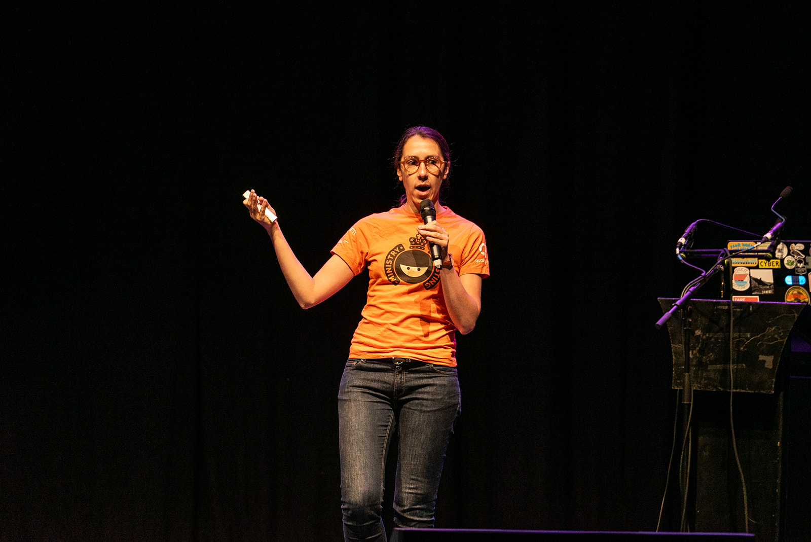 Elizabeth Zagroba speaking on the MoTaCon stage with an orange retro MoT tshirt.