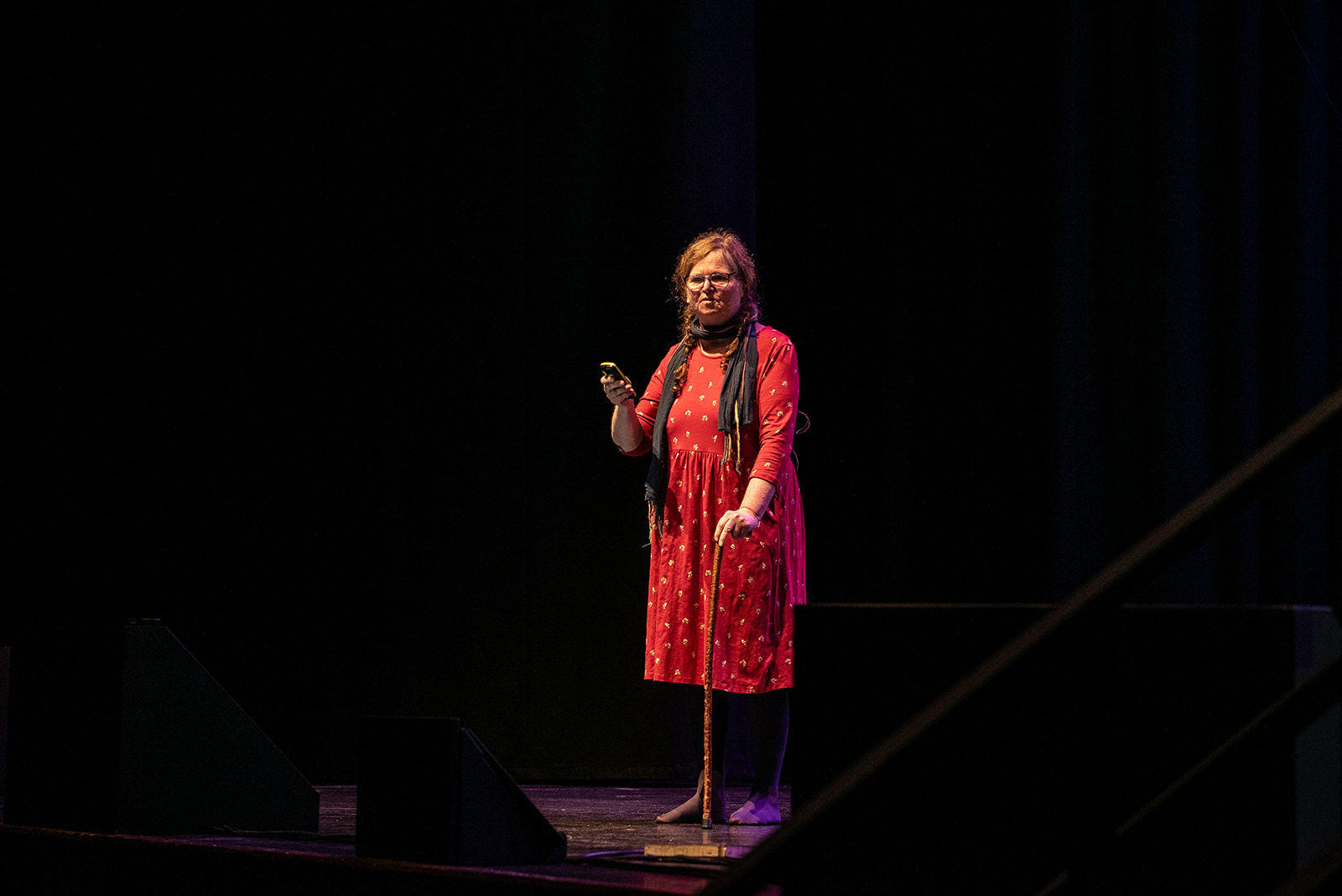 Isabel Evans on stage, wearing red, and surround by a dark no light background.