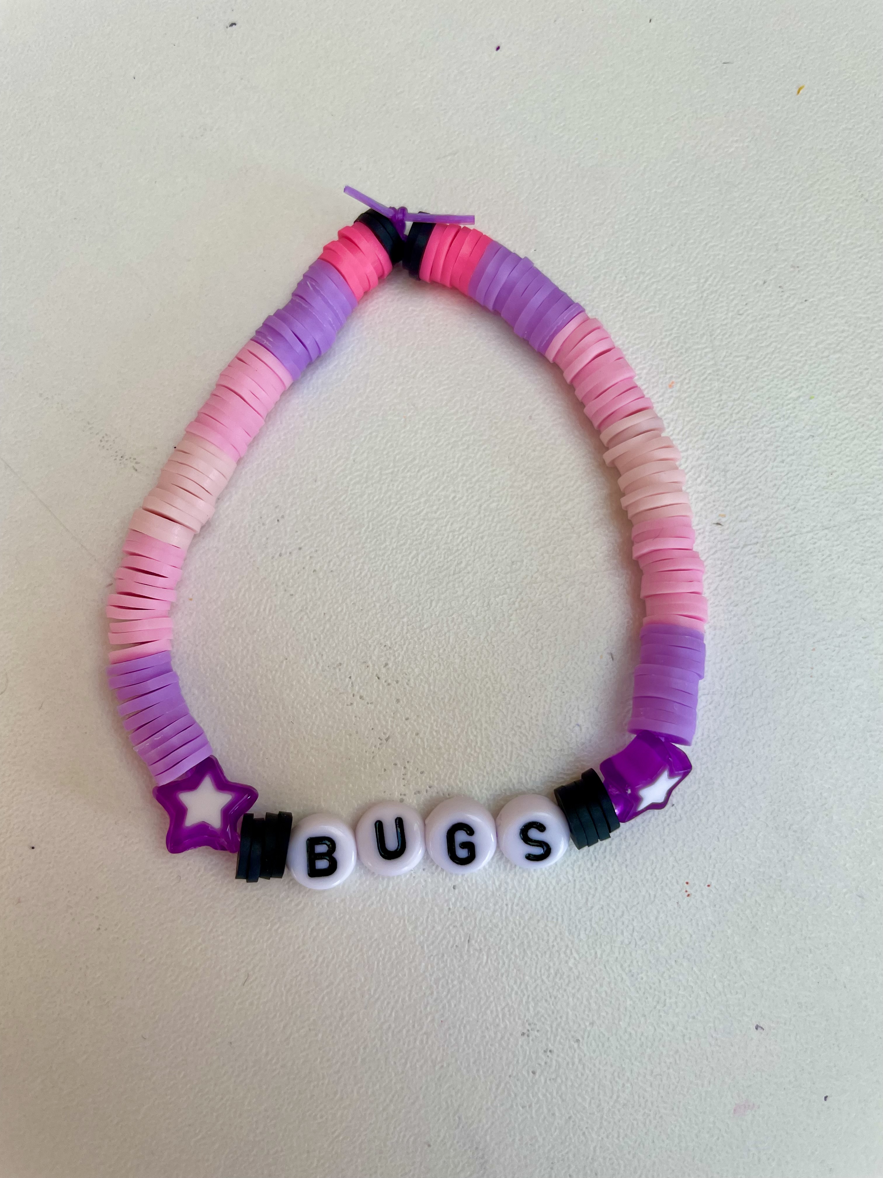 A pink, purple braclet with two stars and the word 'bugs' on it.