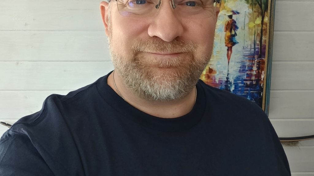 Image of David Williams aka TheTestingMuse, wearing a navy t-shirt with Motaverse lettering in rainbow colours, happy... image