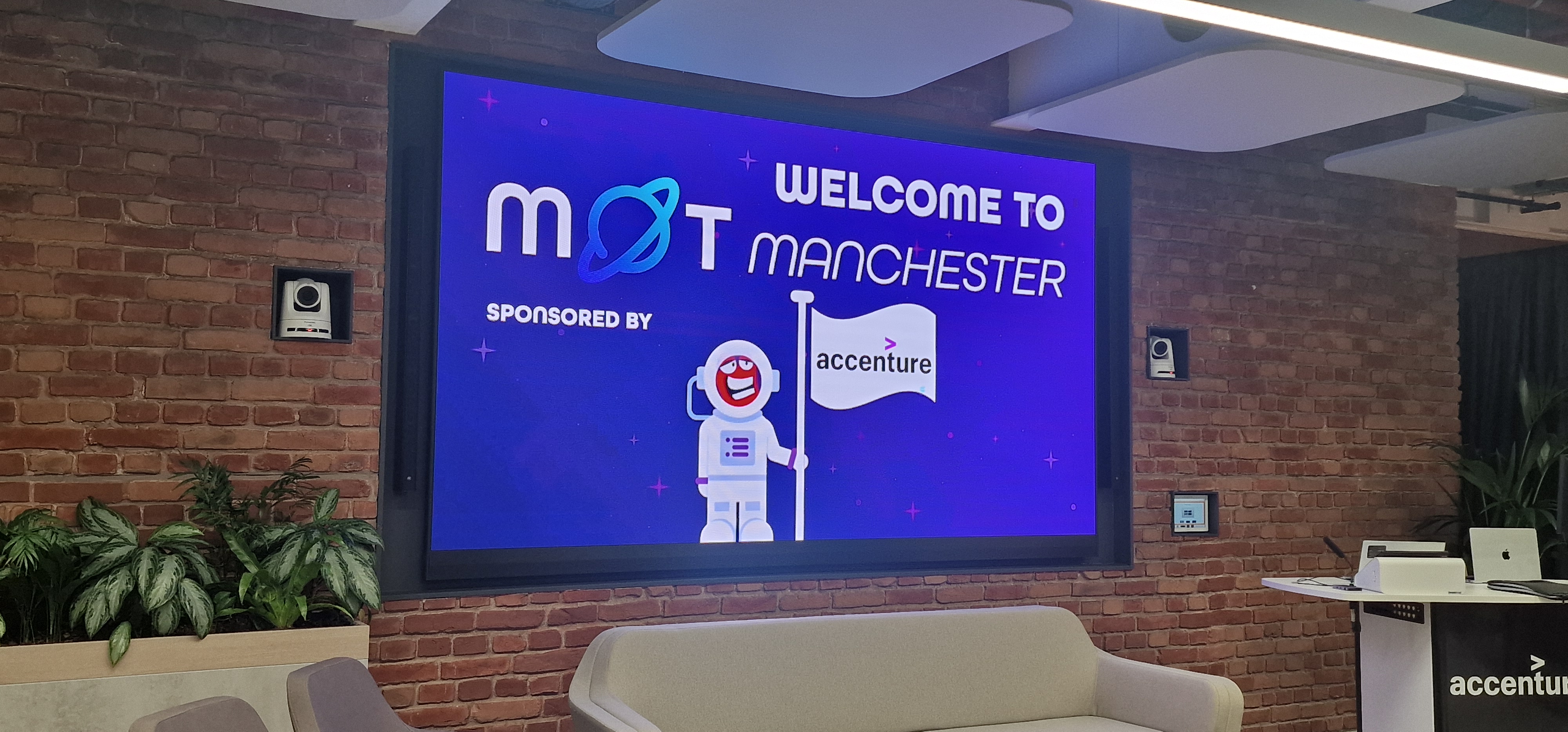 A photo of a large digital screen mounted on a brick wall in a modern office space. The screen displays a purple, spa... image