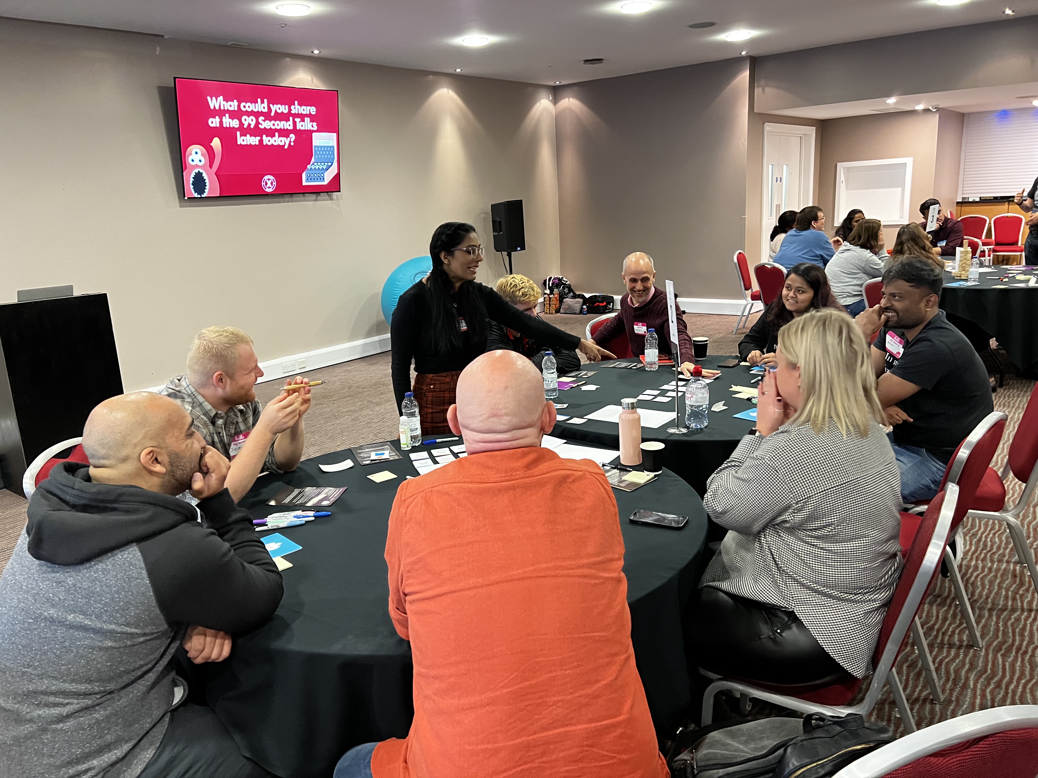 A group of people are gathered around a round conference table, engaged in a discussion during a workshop or presenta... image