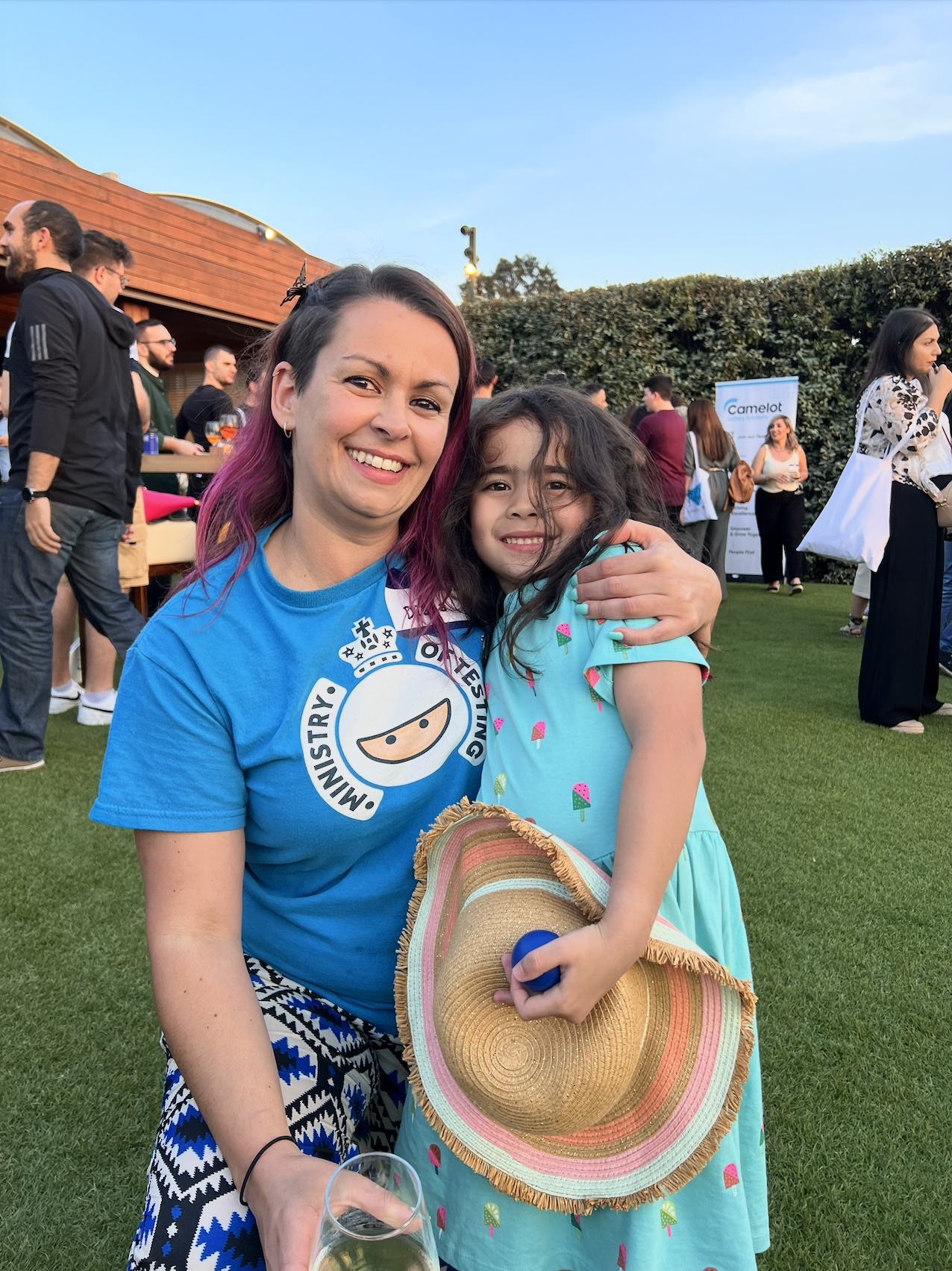 A woman and a girl are smiling for the camera. A few people are socialising in the background.