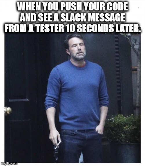 A man wearing a blue sweater and jeans, holding a cigarette, stands outside with his eyes closed and an expression of frustration or exhaustion. The text above reads, "WHEN YOU PUSH YOUR CODE AND SEE A SLACK MESSAGE FROM A TESTER 10 SECONDS LATER.