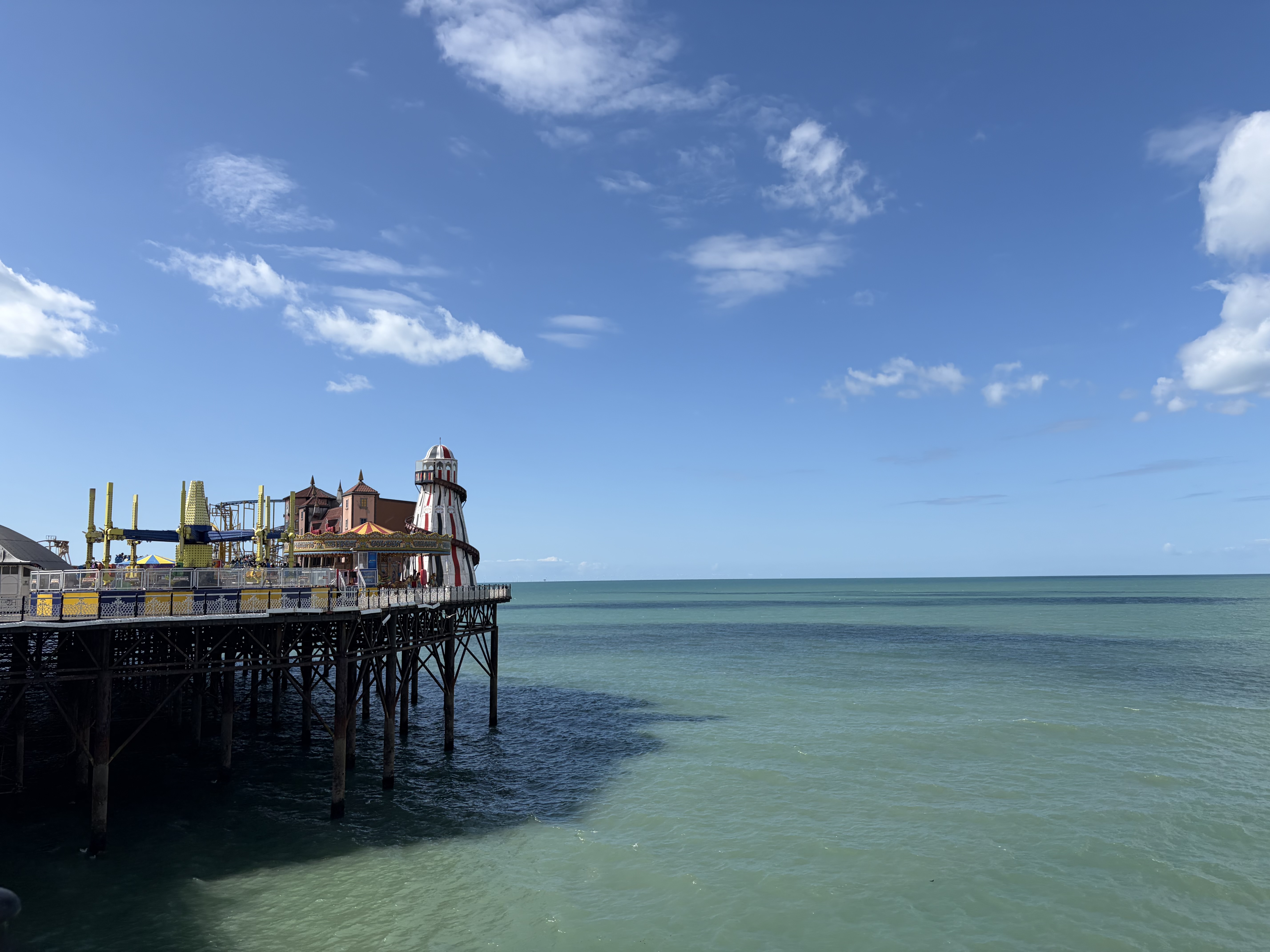 Photo of blue sky and sea at Brighton Palace Pier. There are fun fair rides to the left. image