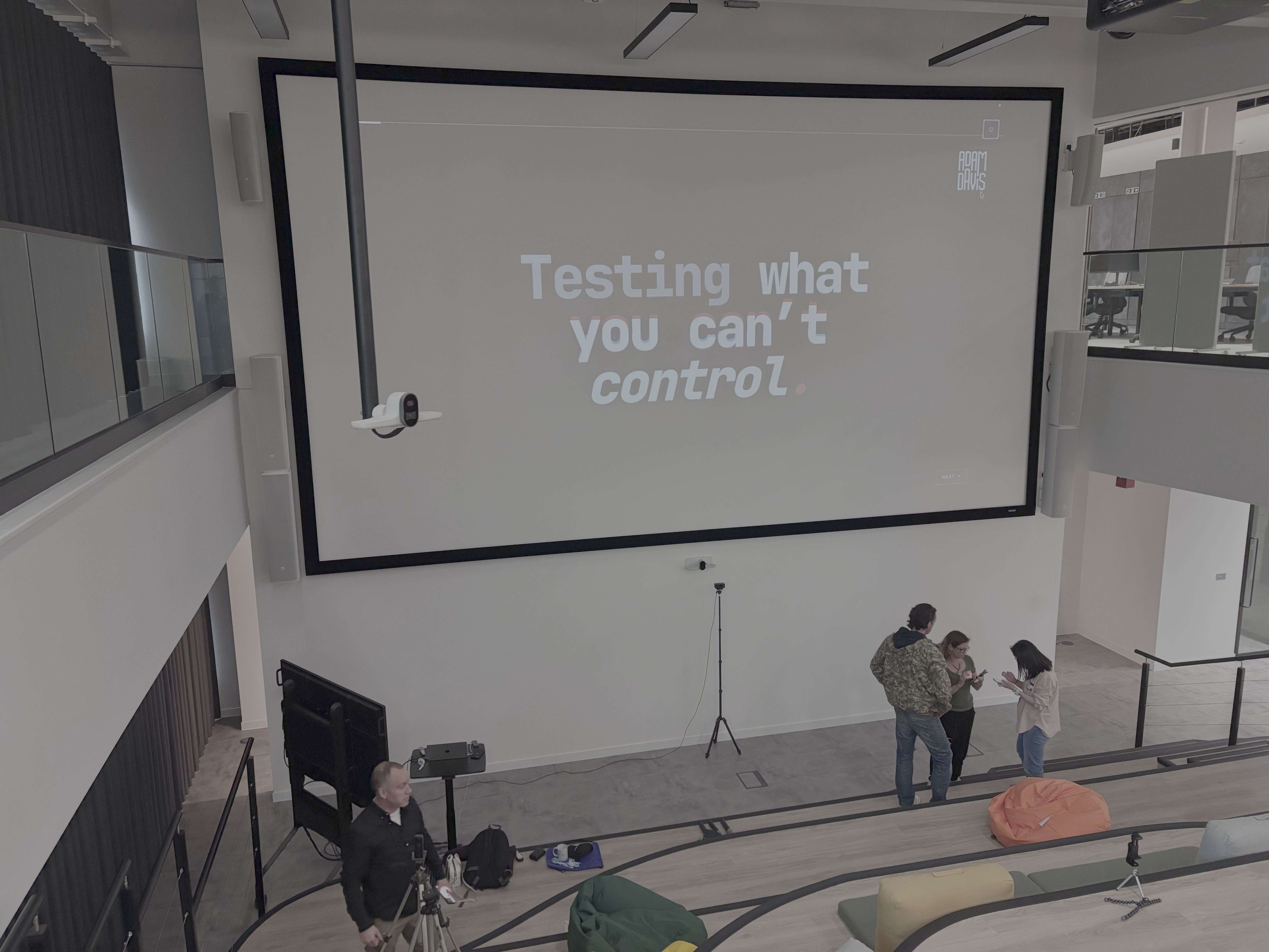 A wide-angle, high-angle shot of a modern presentation space with tiered seating. A large projection screen displays ... image