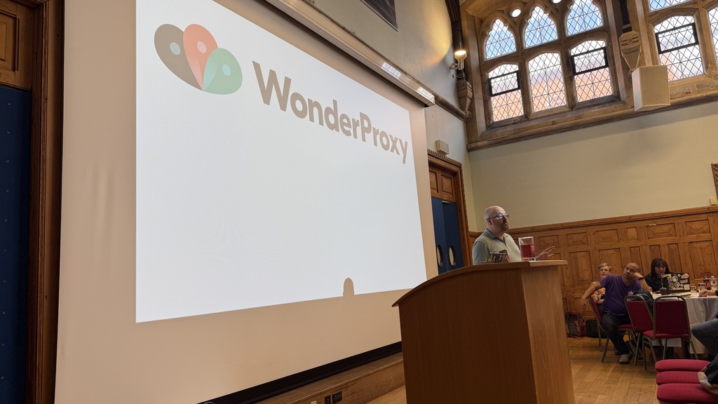 A man speaking in front of a large screen. The WonderProxy logo is displayed.  image