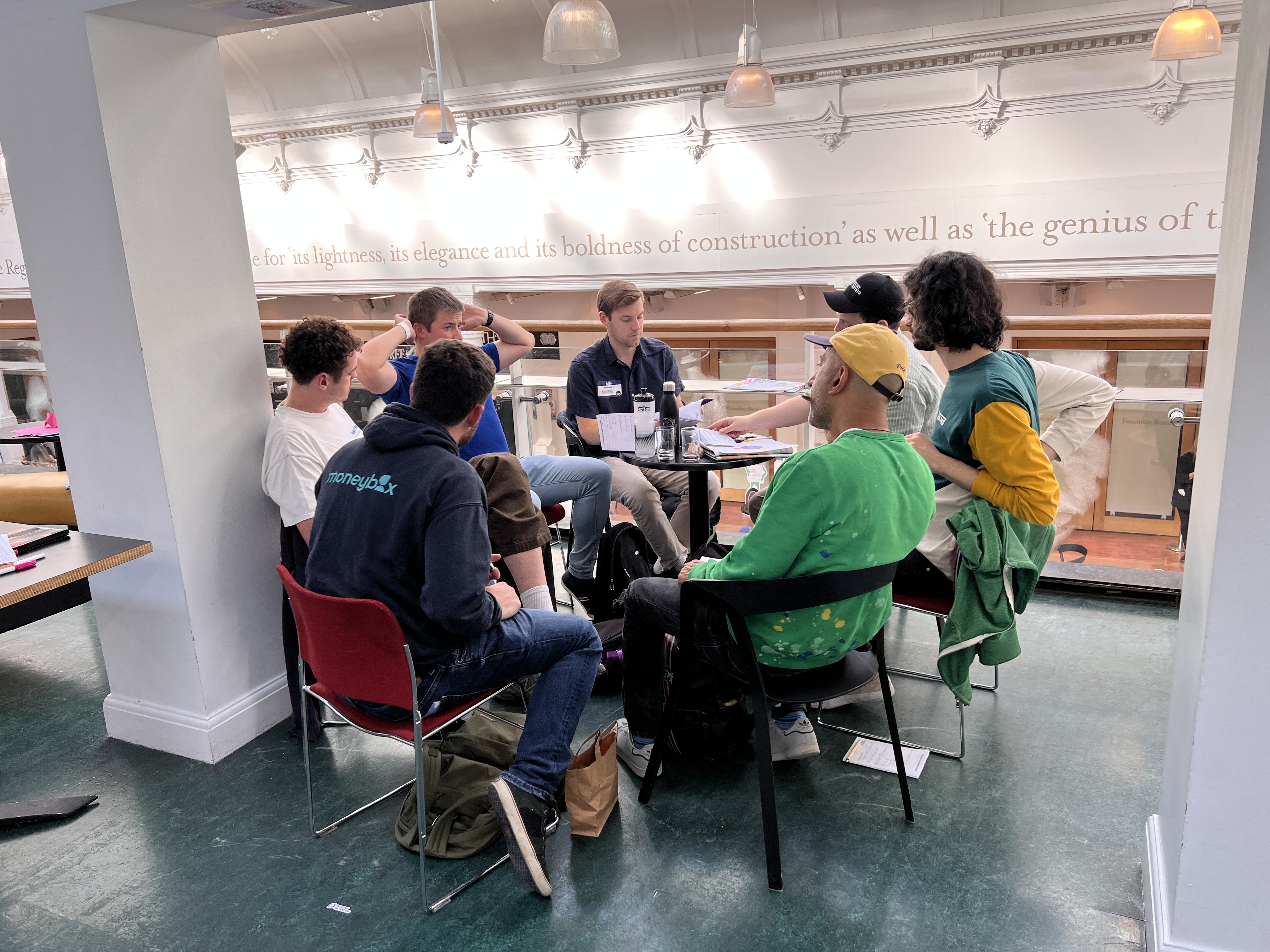 A group of people sitting in a circle of chairs having a collaborative group discussion around small tables. In the f... image