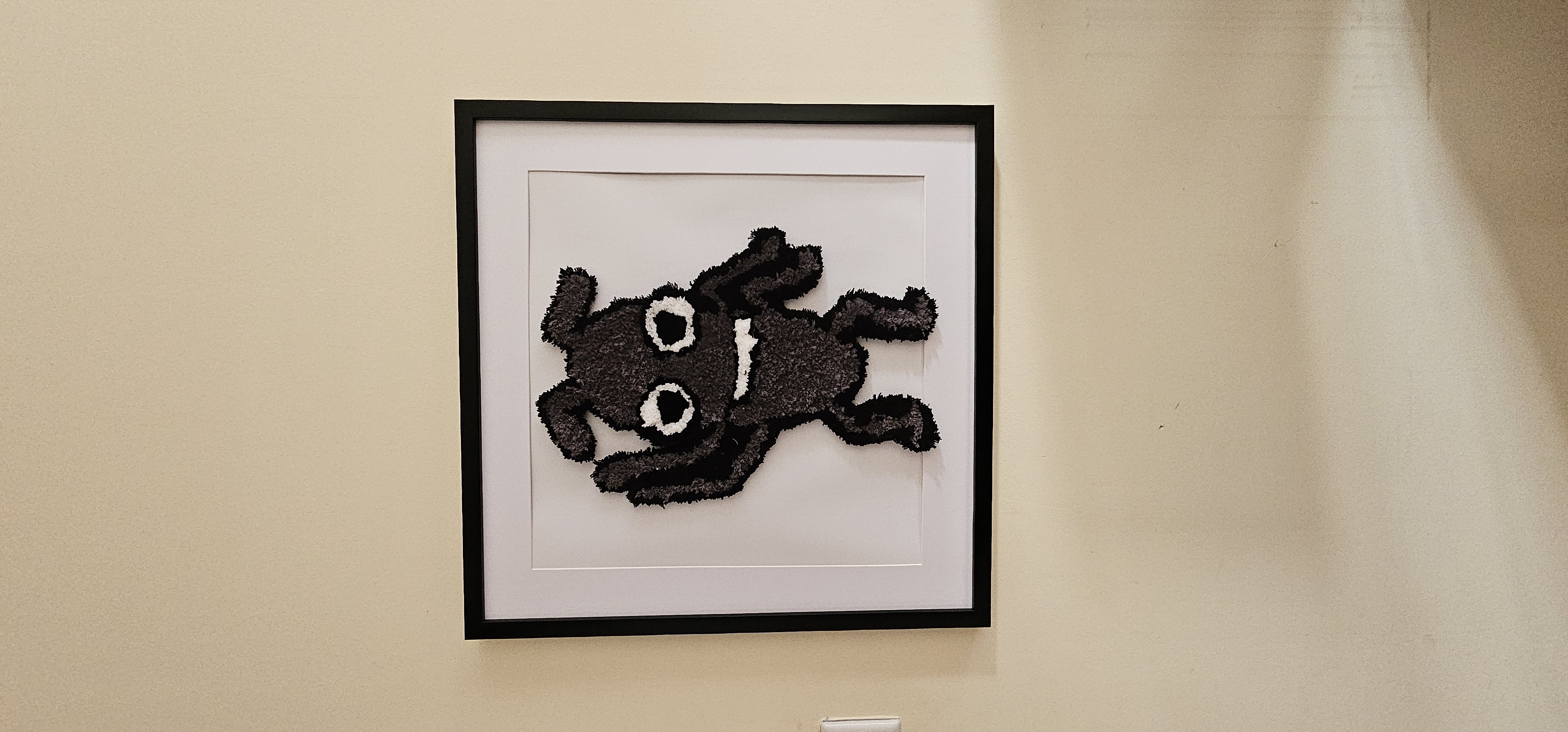 A rug of an animated bug character on a black frame on a white wall.