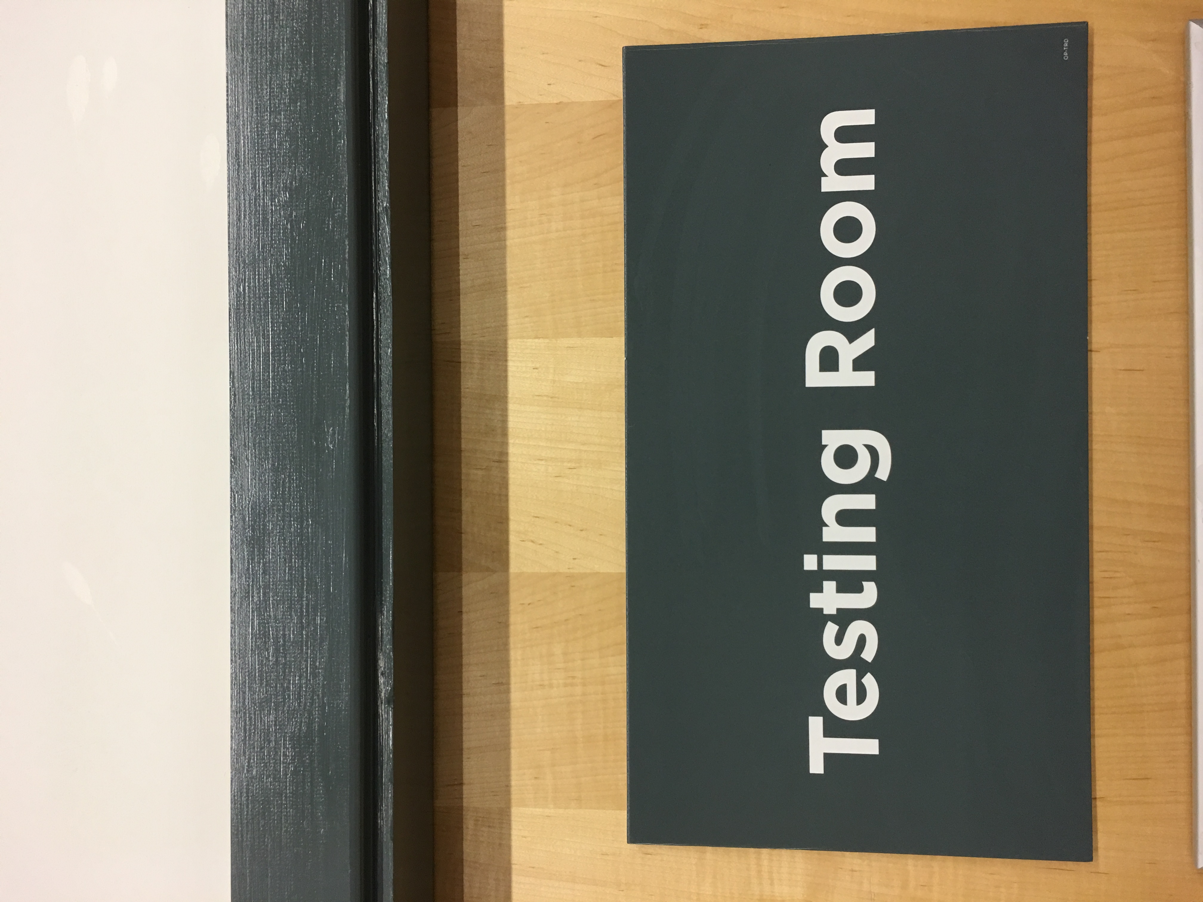 A close-up of a sign on a wooden door. Text: Testing Room 