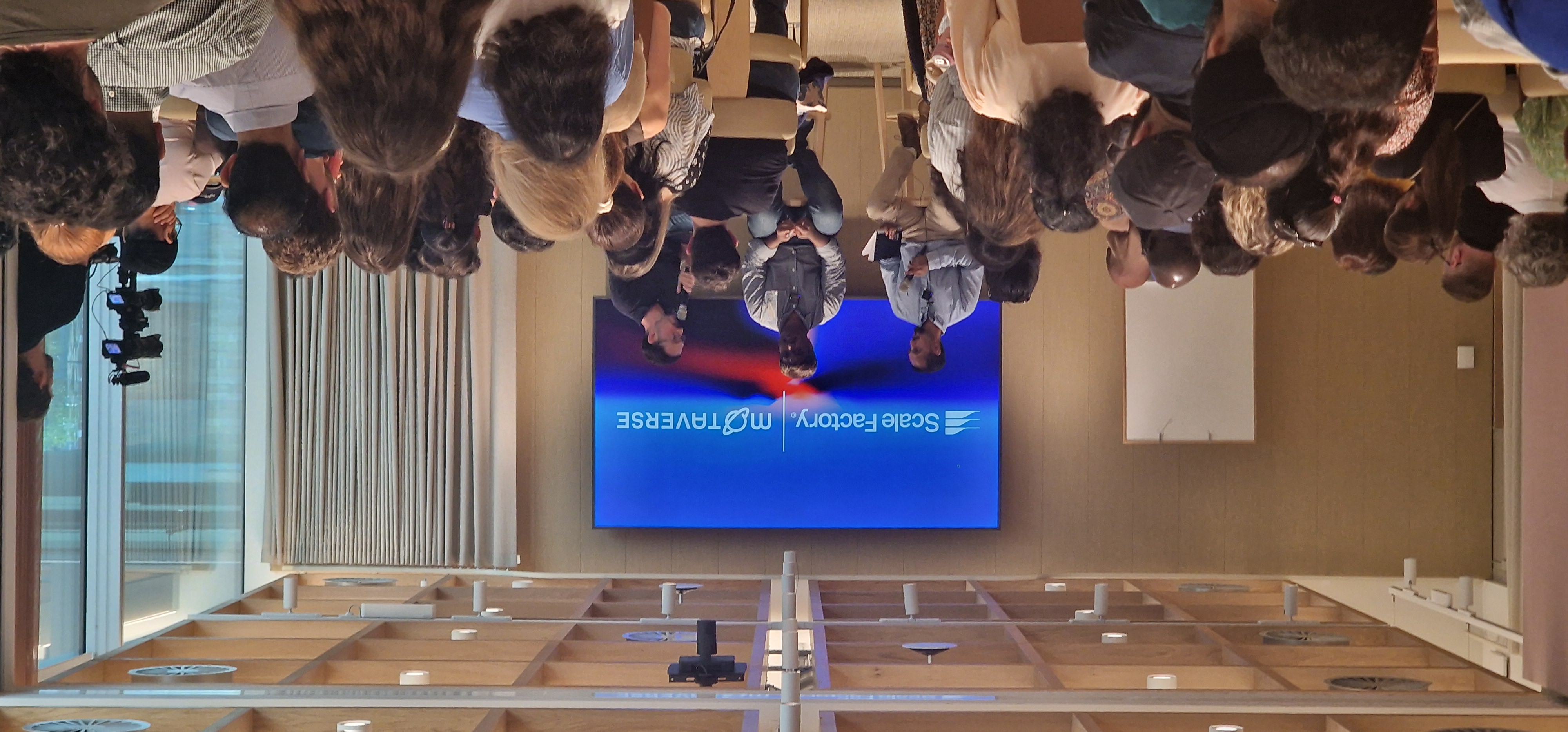 A panel discussion featuring three speakers seated on stools facing a large audience. Behind the panel, a large scree... image