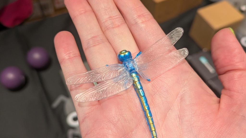 Hand holding a blue dragon fly bug toy hovering over the epic swag table.  image