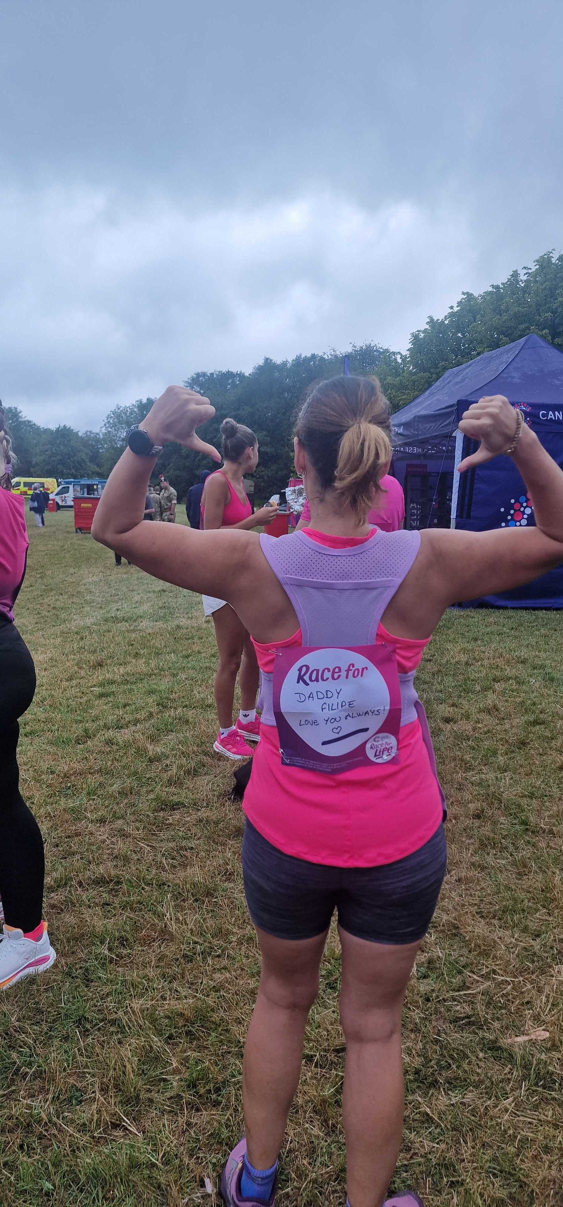 Runner seen from behind at a Race for Life event, wearing a pink vest with a race back sign reading 'Race for Daddy F... image