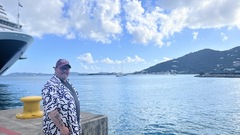 Ady Stokes wearing an MoT planet logo on the dock at the British Virgin Isles. There’s the from of a cruise ship in the background with the bay stretching across to a hillside.  image