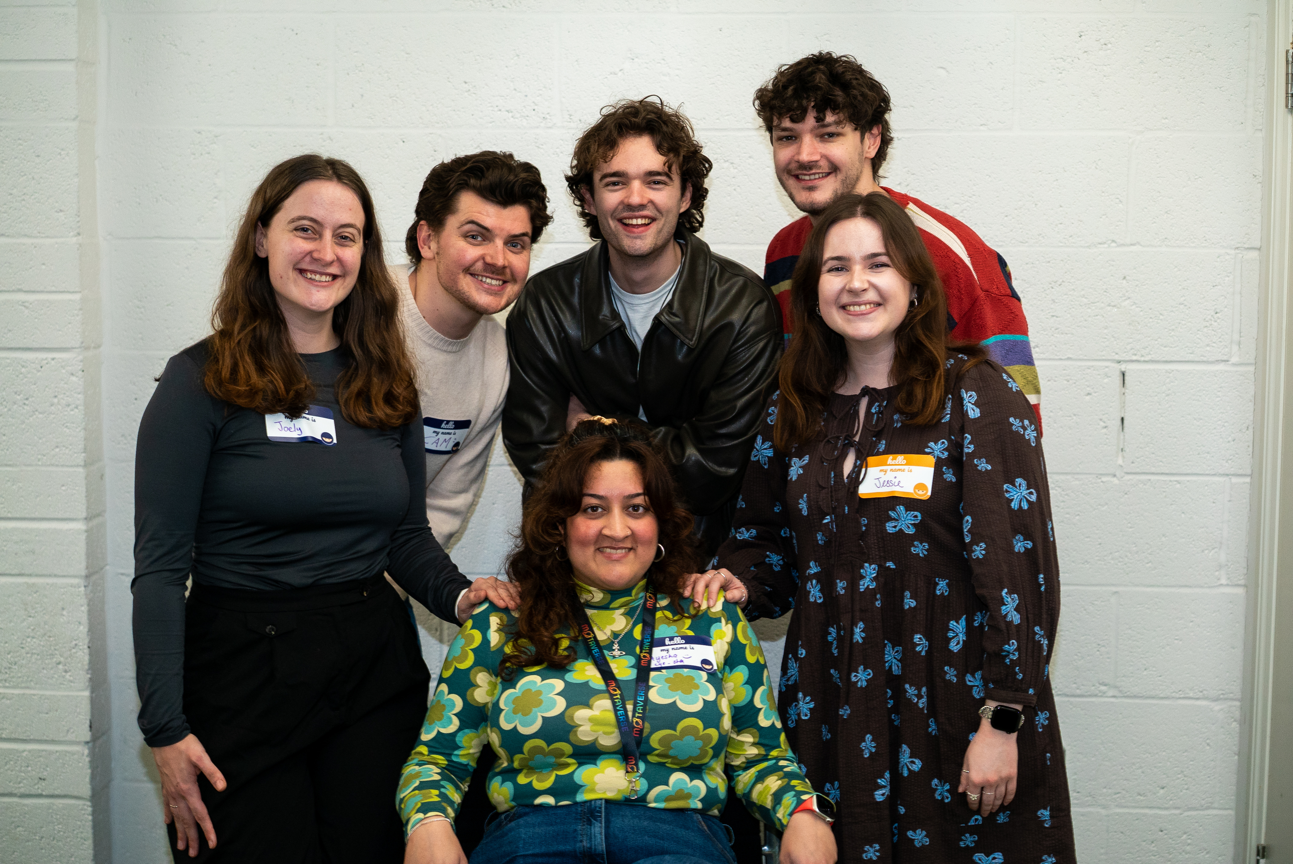 Photograph of Ayesha sat down and Joely, Cameron, Ben, Rowan and Jessie all stood and smiling at the camera. The group had a lot of fun taking this picture in a silly family portrait style. 