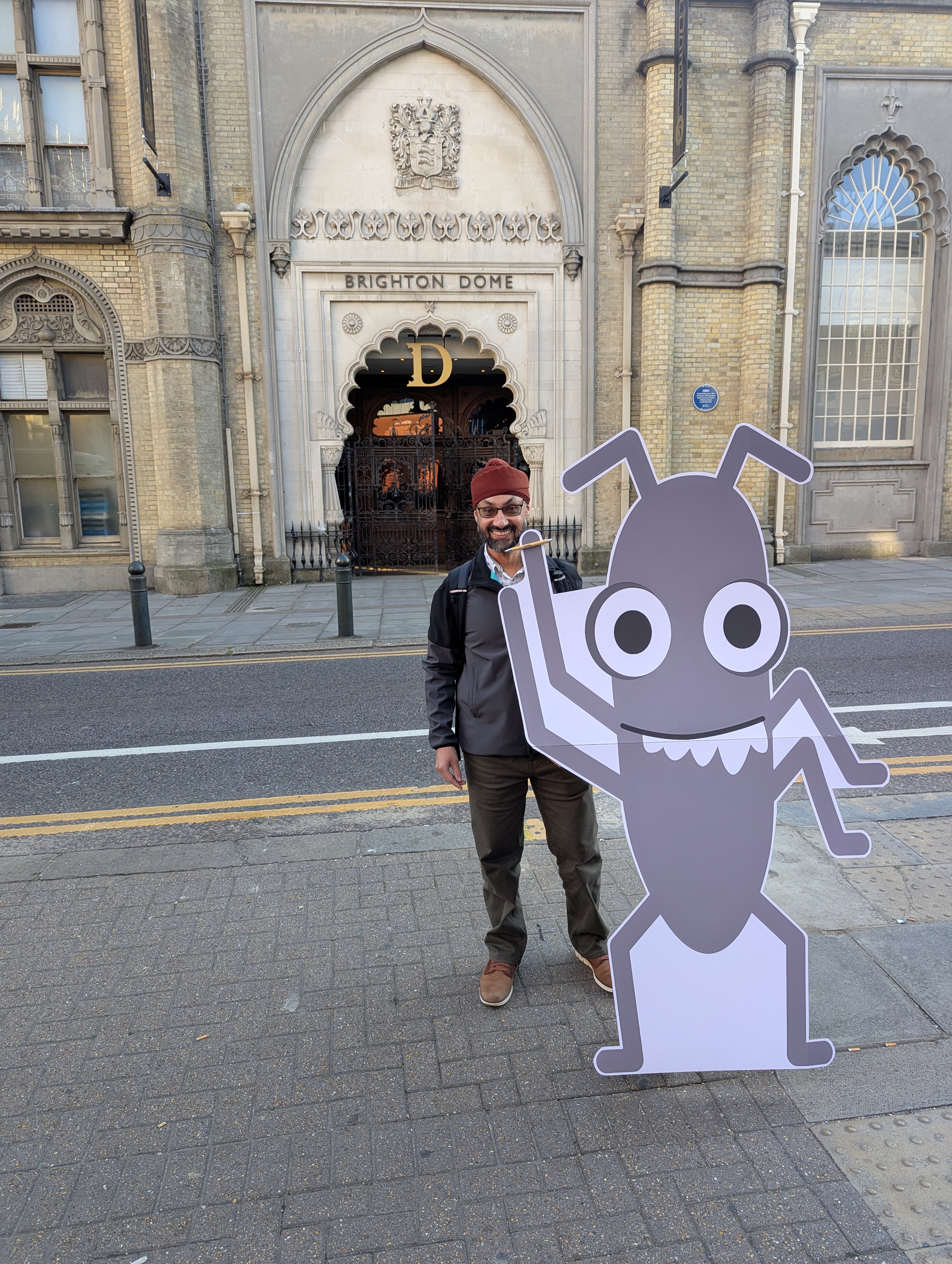 A picture of Dalbir Sehmbi standing next to a Bug - This is the Ministry of Testing mascot