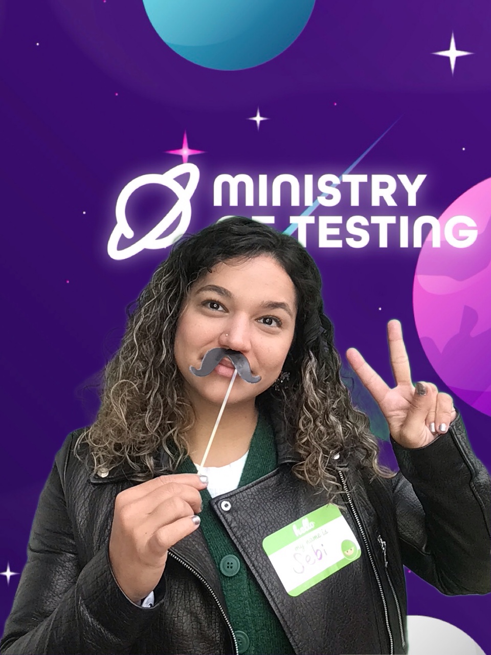 This picture shows a TestBash attendee enjoying themselves in the photobooth. They have a name tag on that says 'Sebi'. Sebi has dark curly hair and is wearing a leather jacket with a fun moustache on a stick held up to their face while they throw up a peace sign to the camera. 

Background: The green screen backdrop depicts a simple illustrated outer space scene. The main colour is purple, with cute stars and planets in shades of pink, blue, and white. About a third of the way down the screen, a logo appears. It reads "Ministry of Testing" in bold white text with a blue shooting star behind it. Next to the text, in the same bold white style, is a line drawing of the planet Saturn.