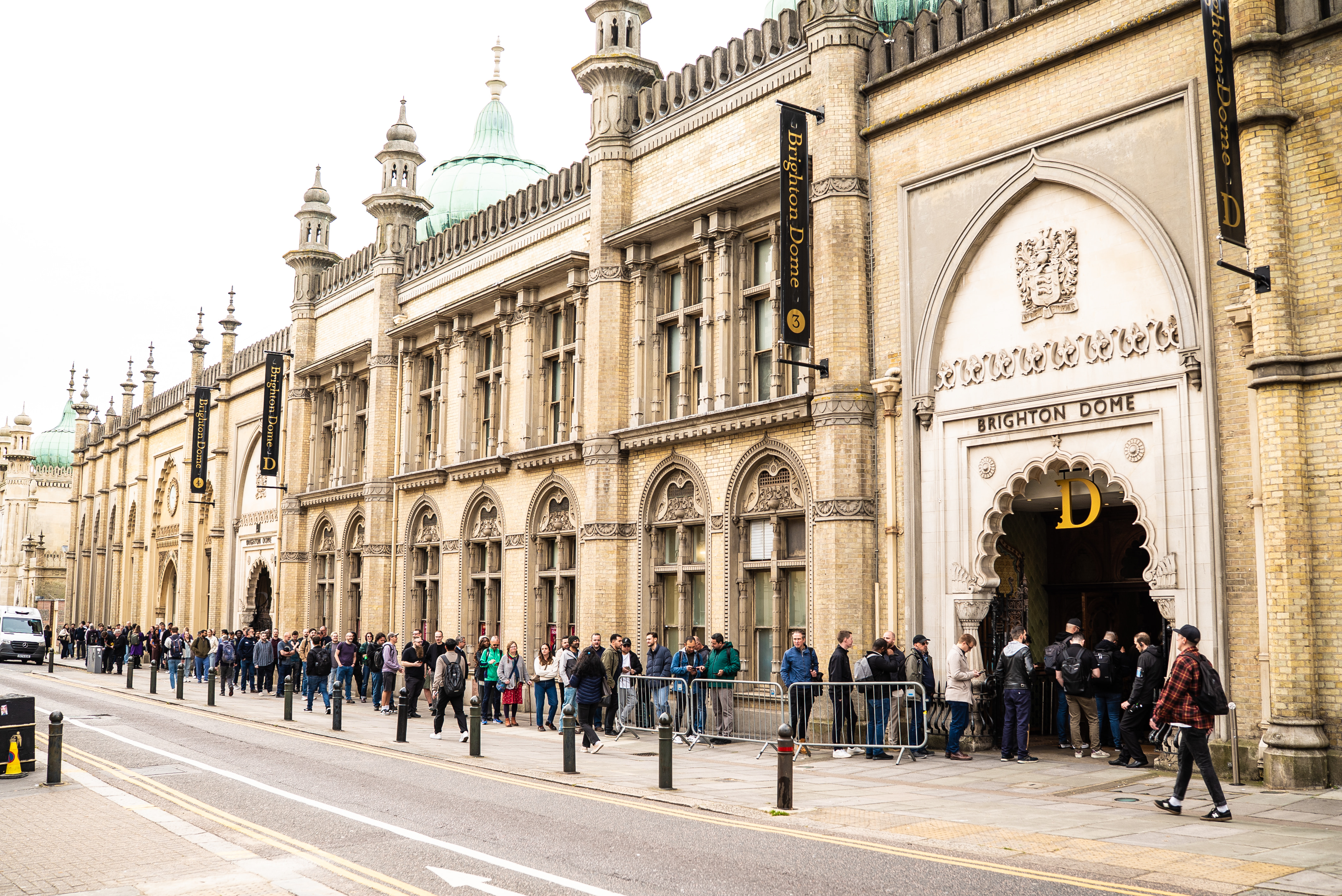 A long queue of attendees stretches along the pavement outside the historic, Indo-Saracenic style facade of the Brigh... image
