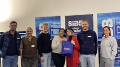 A group photo from the Ministry of Testing (MoT) Berlin meetup held at the SIBB Startup Incubator. Seven individuals are standing in front of banners with SIBB branding. One person holds a purple b... image