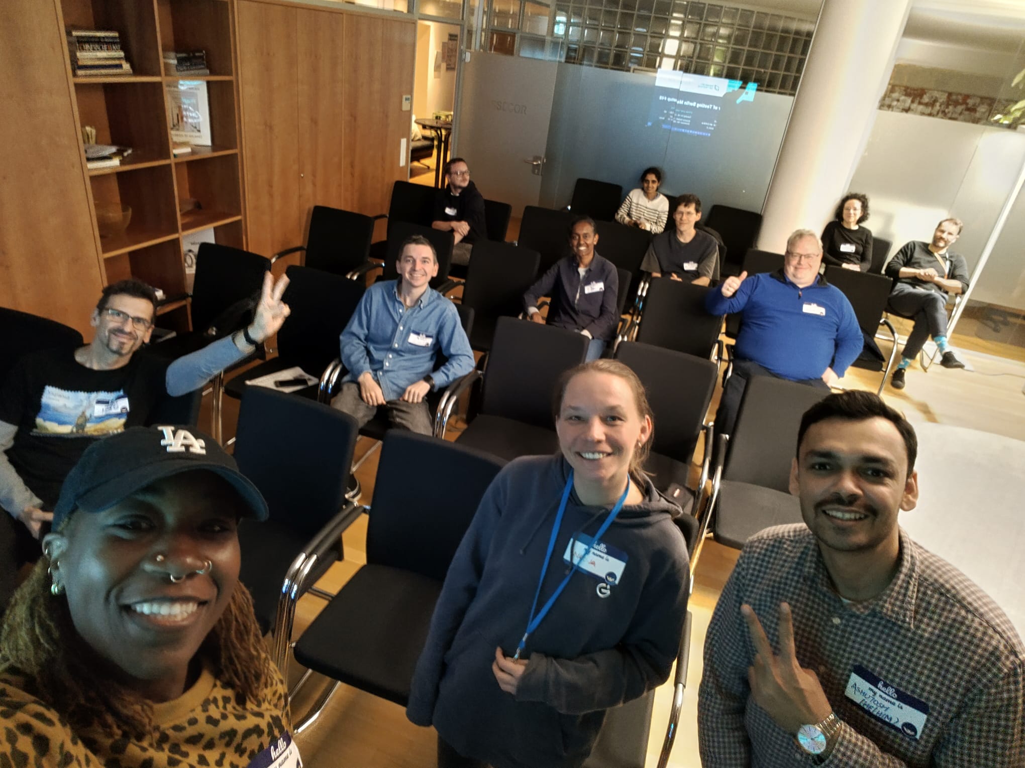Ash, Nadja and Ashutosh taking a selfie with the MoT Berlin meetup audience. The room has black chairs lined up, half of them occupied. The audience looks happy and ready for more! 