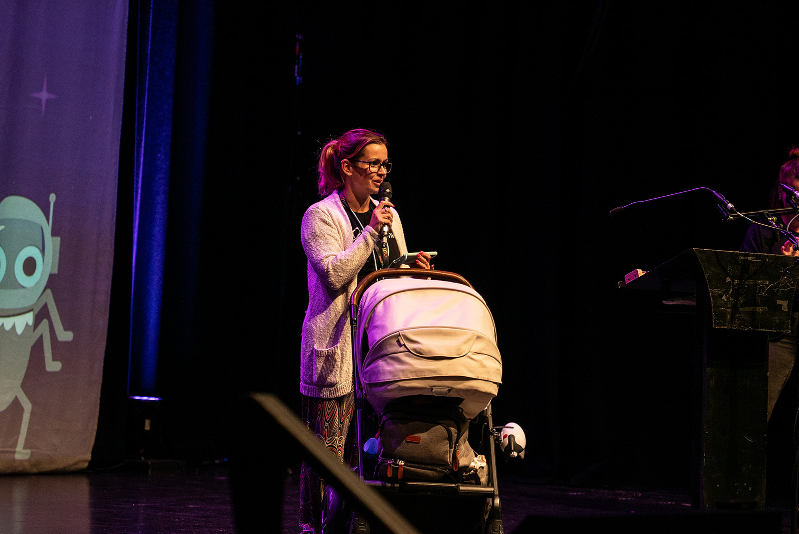 Diana Dromey on stage doing a 99 second talk with Baby Cai on stage in a light coloured buggy.