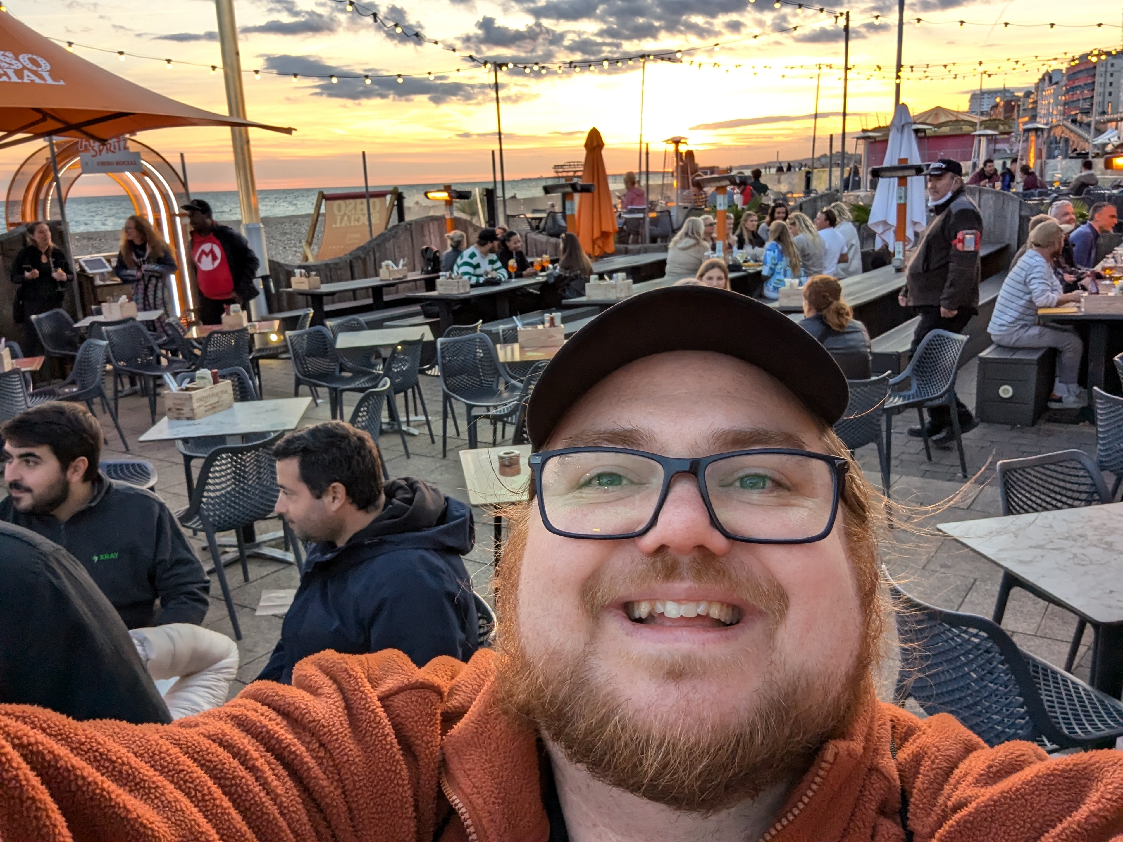 Ben Dowen taking selfie with other TestBash attendees in the background socialising and a sunset at OhSocial