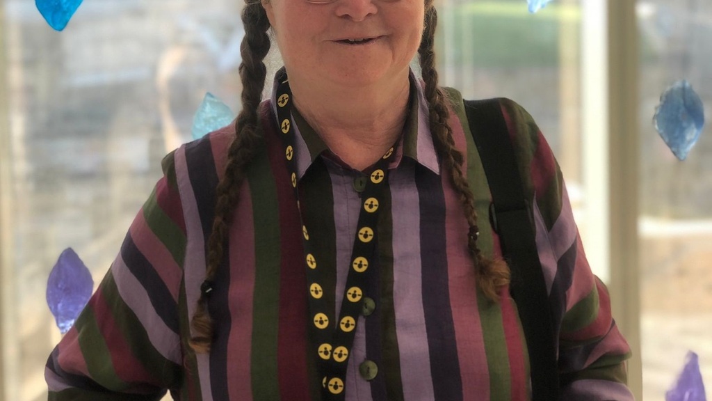 Photo of Isabel, standing and smiling. I'm 70,  female, walk with a stick, I've got one or two plaits depending on mood.