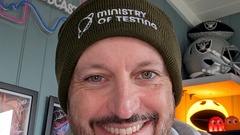 White male in a grey hoodie sitting at a desk wearing an olive green Ministry of Testing beanie in his head image