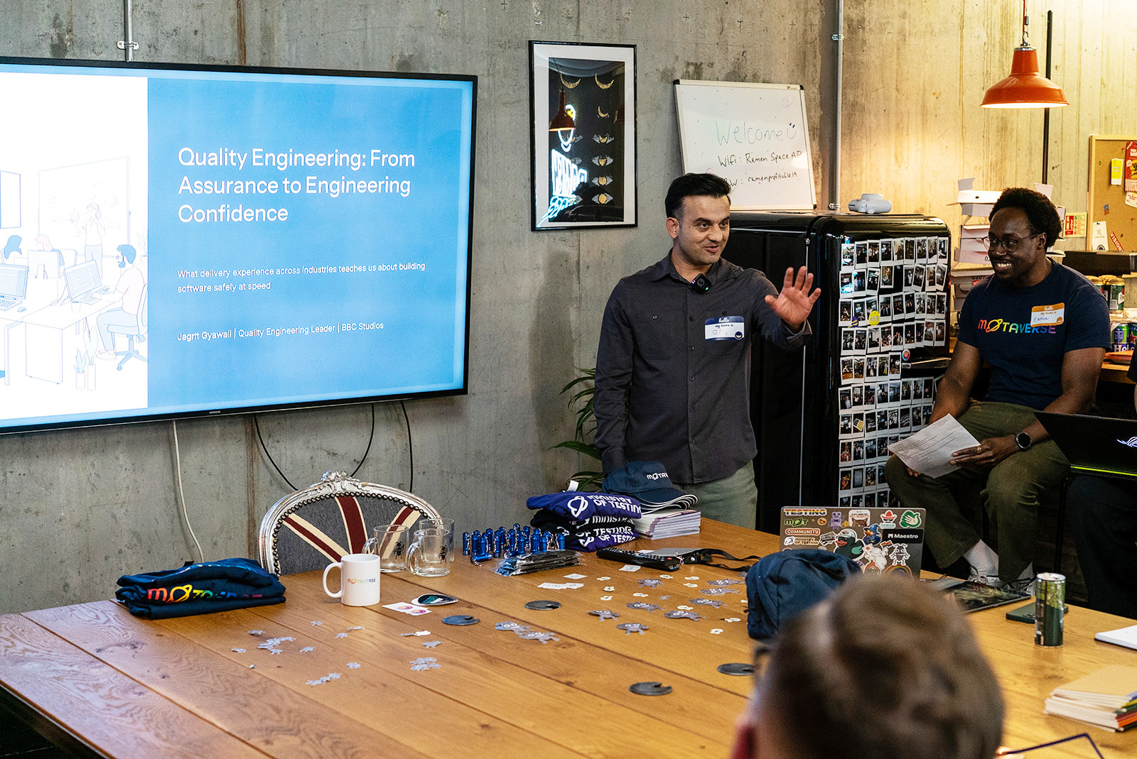 A photo of Jagrit Gyawali delivering his talk at MoT London. Jagrit is talking next to a display showing his presentation.