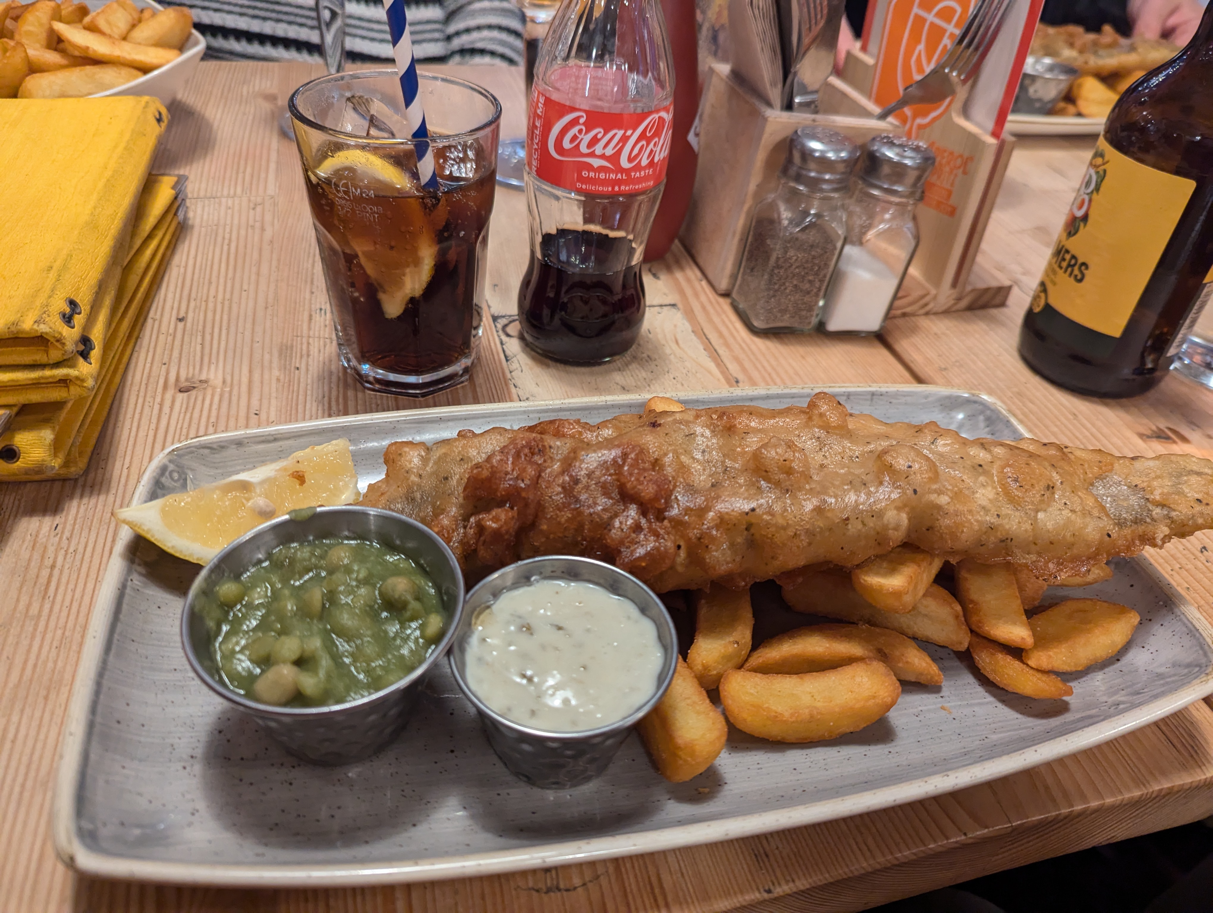 Plate of food, bettered fish, peas, with a coke in the background