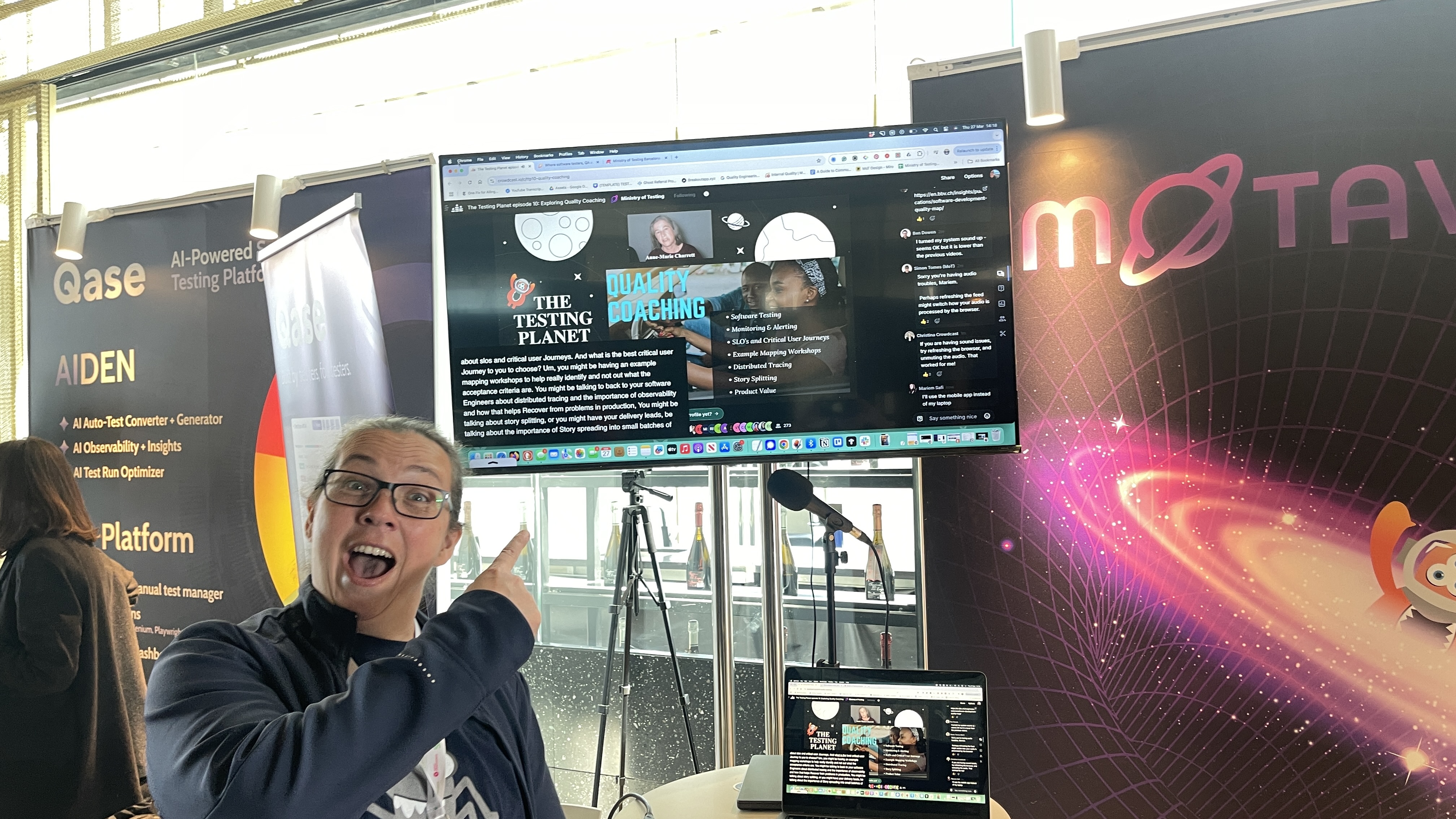 Rosie Sherry points excitedly at a monitor displaying The Testing Planet Live season finale, streamed directly from the MoTaverse stand at Selenium Conf 2025. A laptop below mirrors the same screen, and the MoTaverse banner glows behind her.