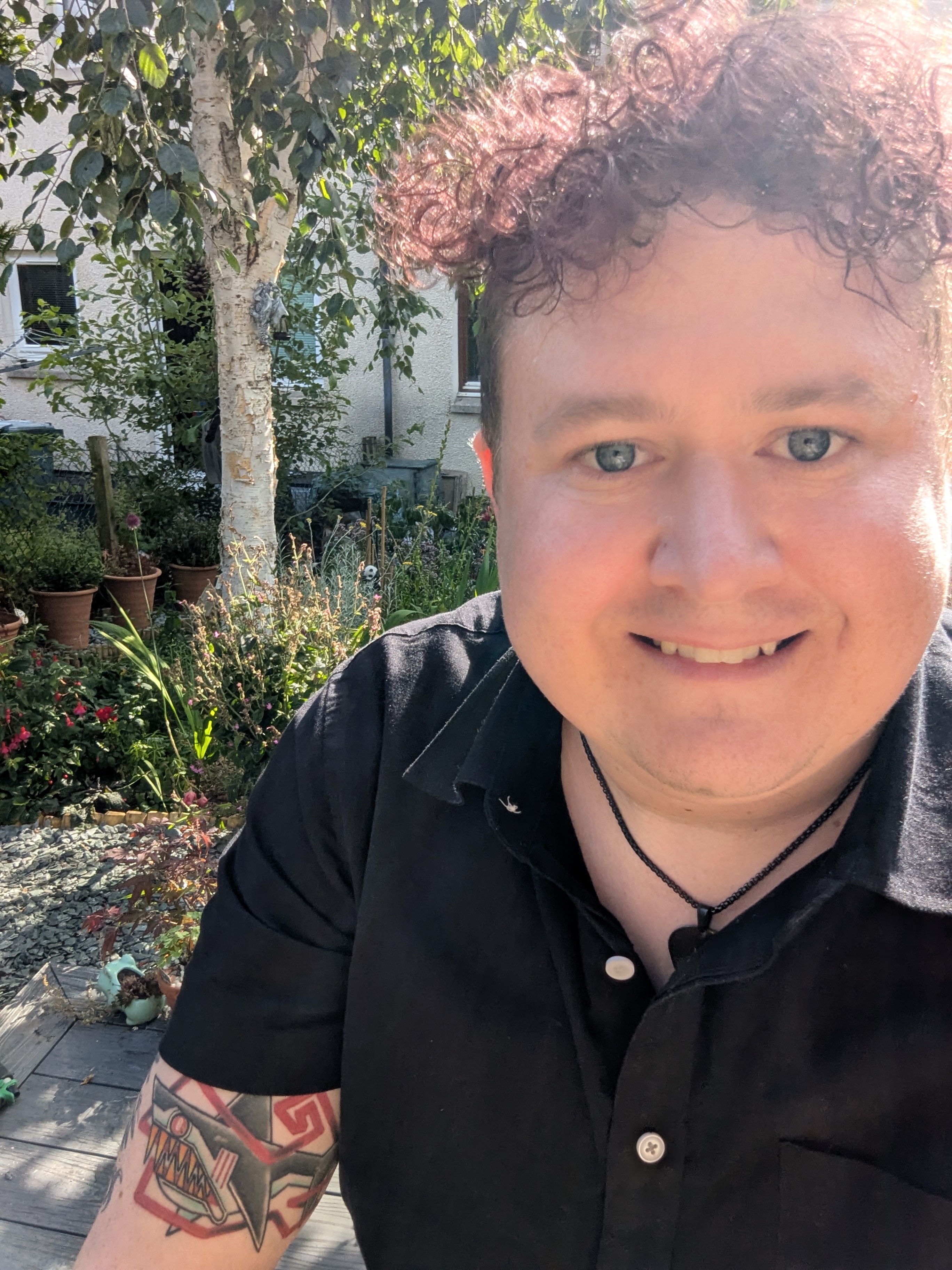 Image of Richard Adams. White male with pinkish reddish curly hair. Sat in garden.