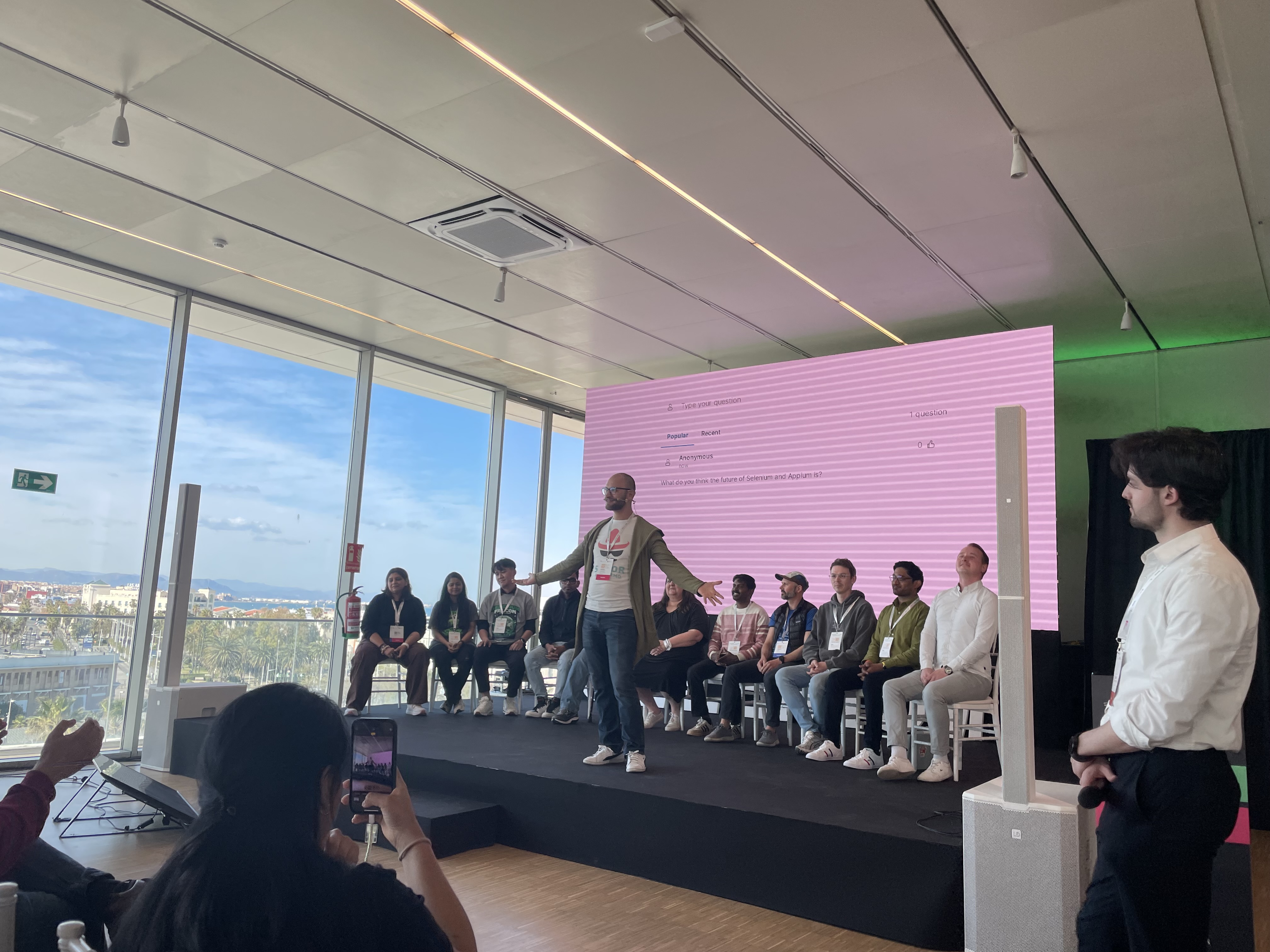 A photo of Leandro Melendez on stage with his arms spread out and the panelists sitting behind him in a line.