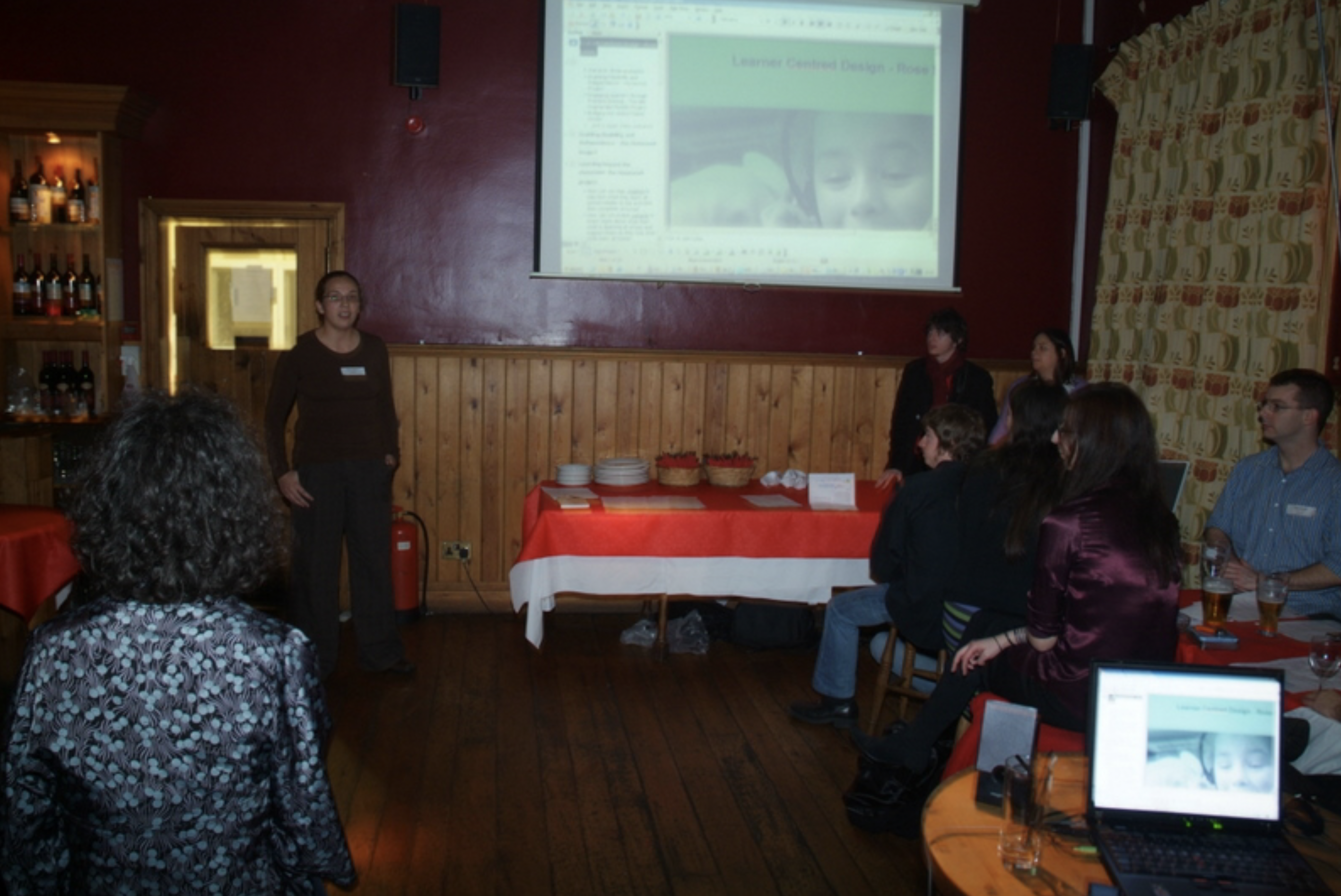 Rosie standing in the front of a room in a pub, saying something at what was a Girl Geek Dinner meetup. image