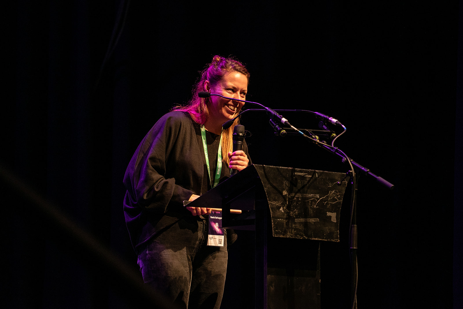 Veerle Verhagen on the MoTaCon stage. She's standing behind the podium with a cheek grin.