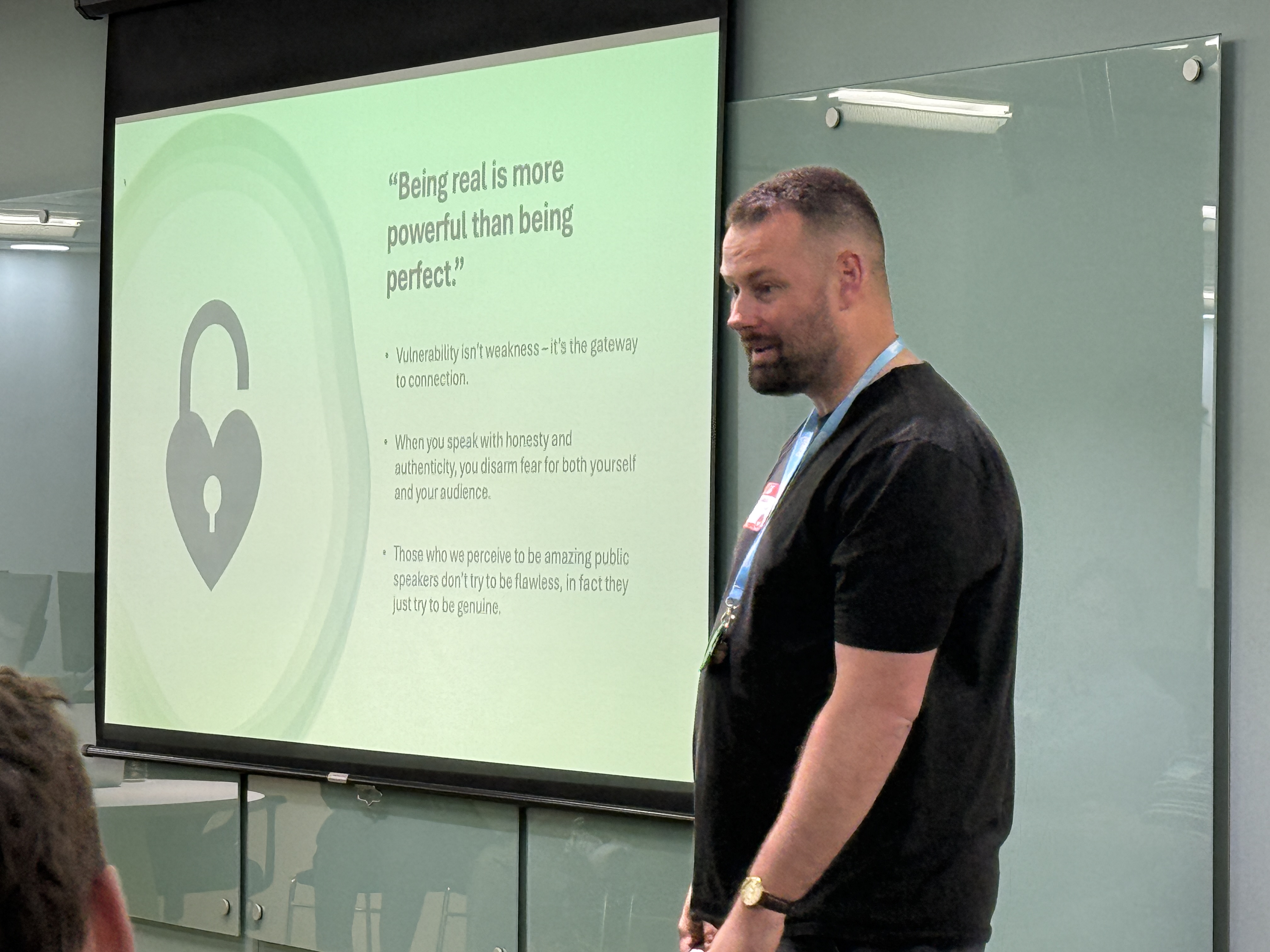 A white man presenting a talk. The slide has a quote on it: "Being real is more powerful than being perfect."