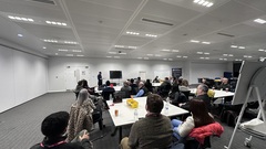 Room of attendees on tables listening to a speaker image