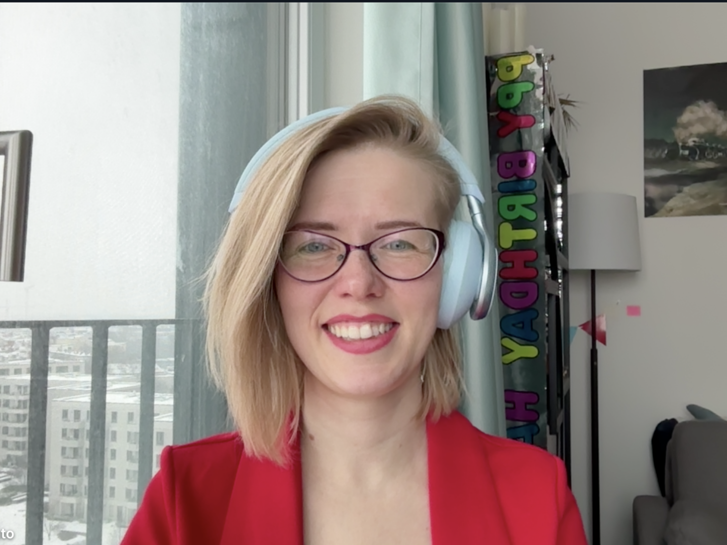 Christine Pinto smiling in a bright room, wearing glasses, a red blazer, and light blue headphones.
