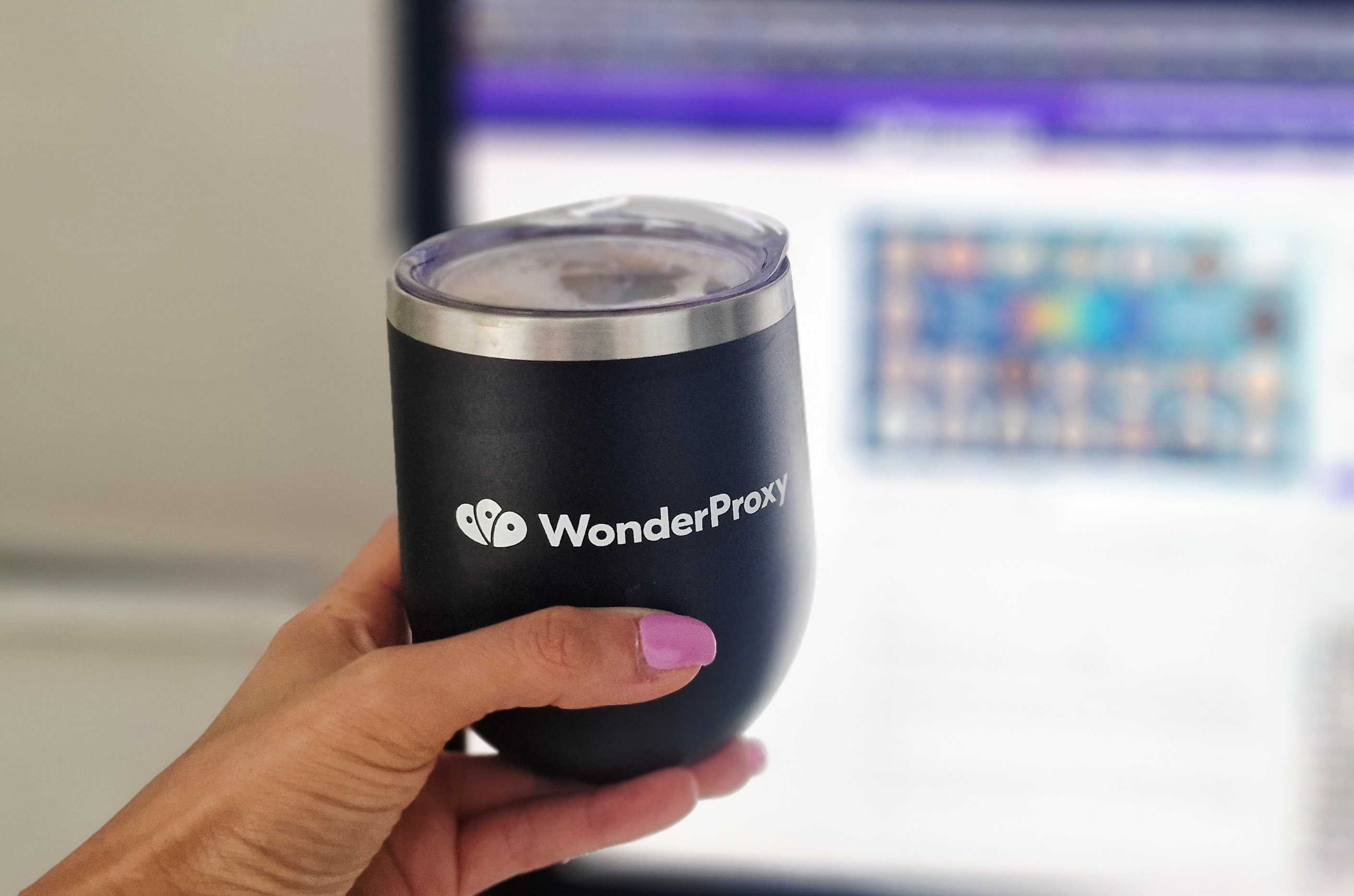 A hand with pink nail polish holds a matte black, rounded insulated tumbler with a clear lid and a silver rim. The tu... image