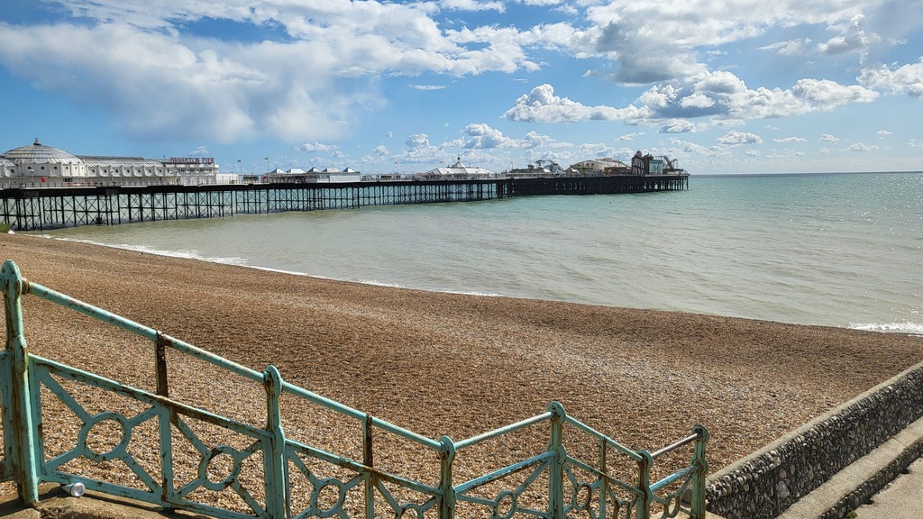 A photo of Brighton Pier, a pebble peach, the sky is blue with some clouds. It was a sunny day.
