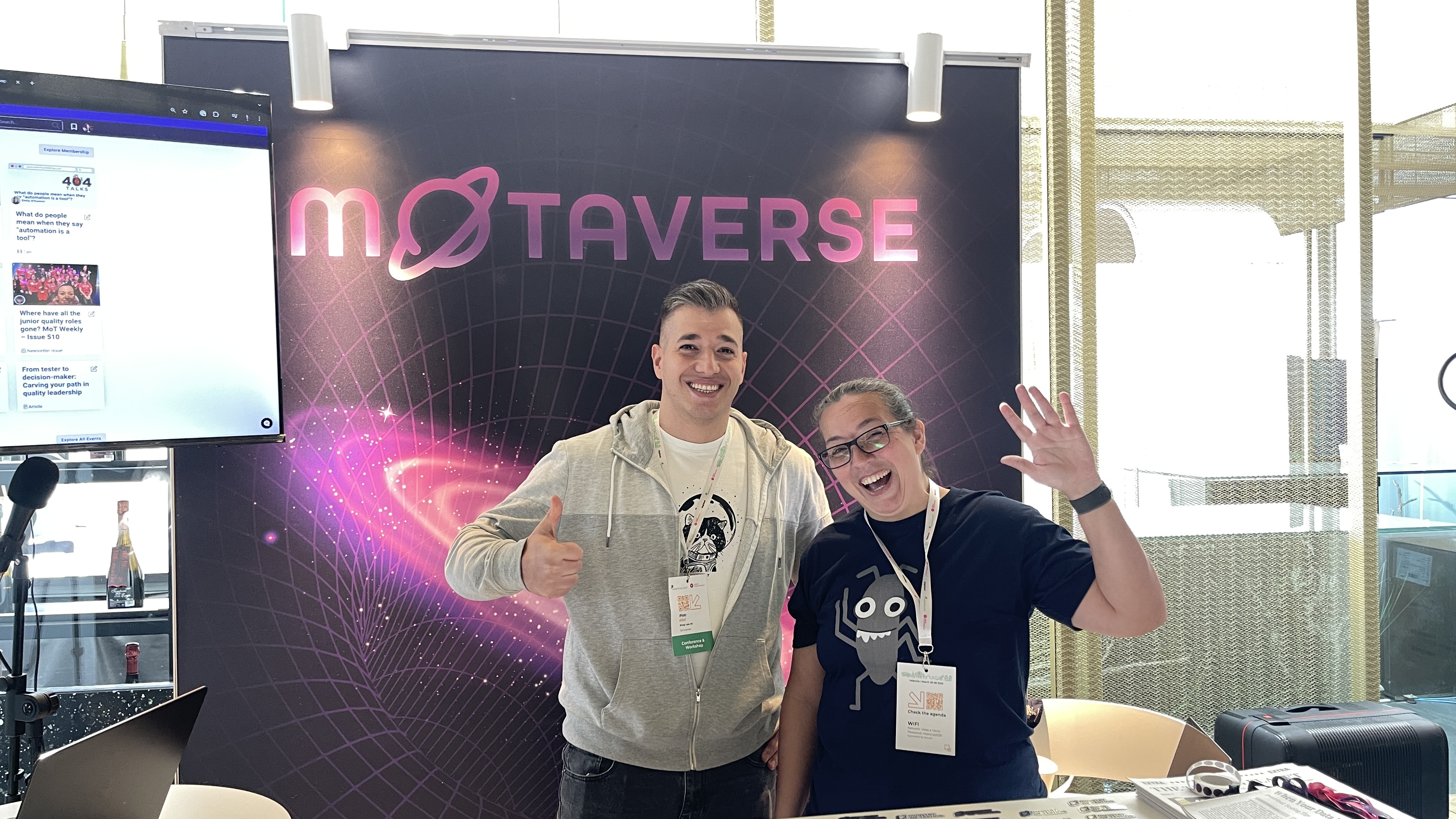An attendee poses with Rosie Sherry at the Ministry of Testing stand at Selenium Conf 2025, both smiling and waving in front of the MoTaverse backdrop. A screen displays community articles to the left.