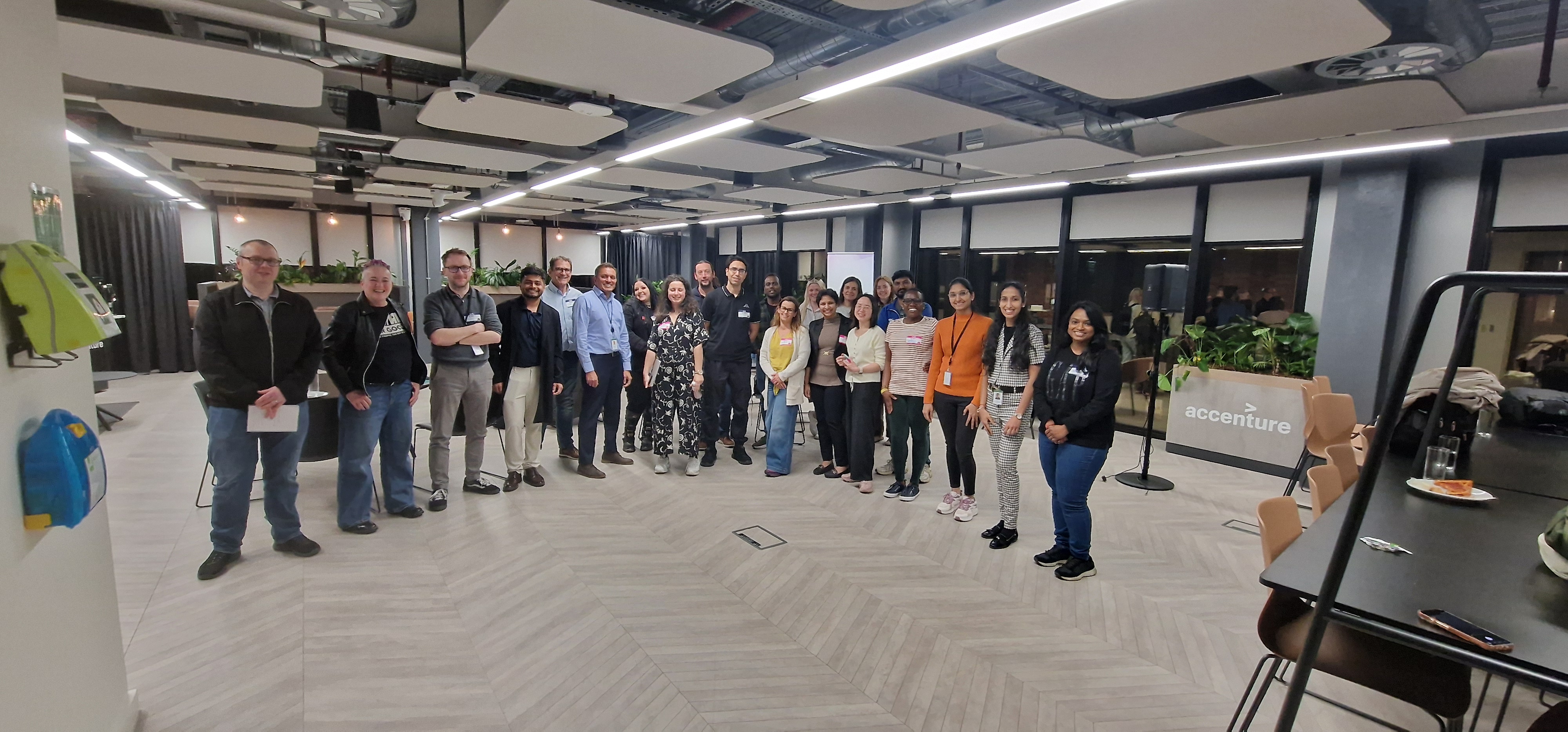 A group of people sitting at black circular tables in a modern office lounge, listening to a presentation. The room h... image