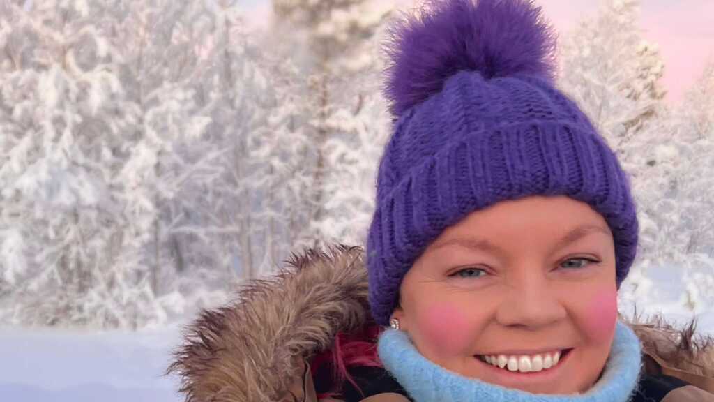 It's a close up picture of me in a thick brown coat with a fur-lined hood. I'm wearing a light blue polo neck and hav... image