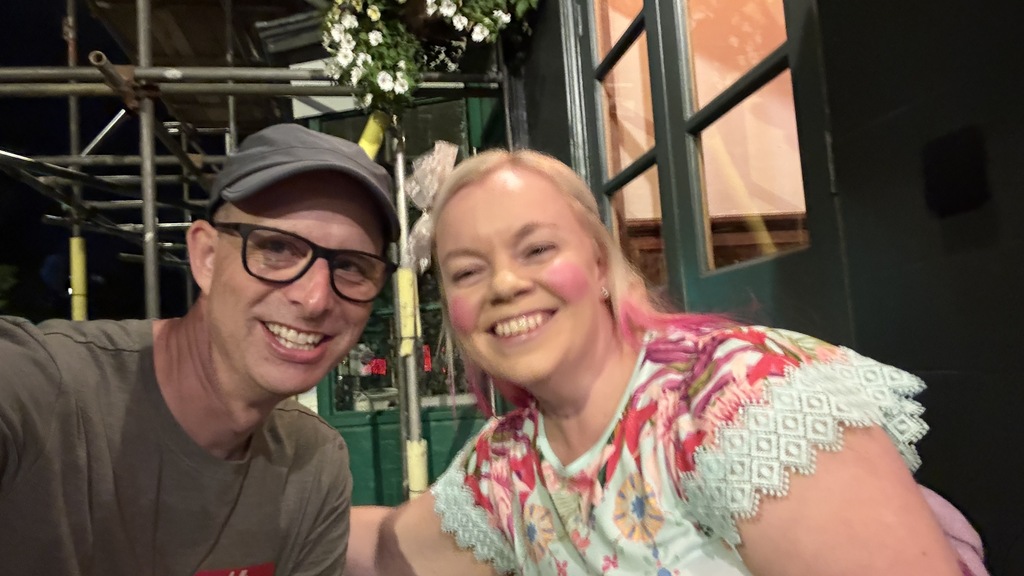 A man and woman pose for a selfie sat outside a pub. image