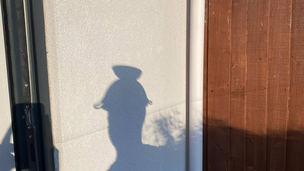 Shadow of a person wearing a colander on their head.  image