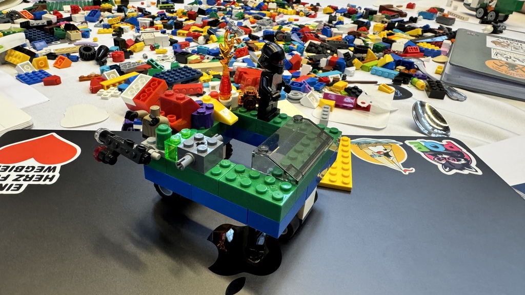 A colorful LEGO creation sits on a table covered with hundreds of loose bricks and pieces. The build resembles a smal... image