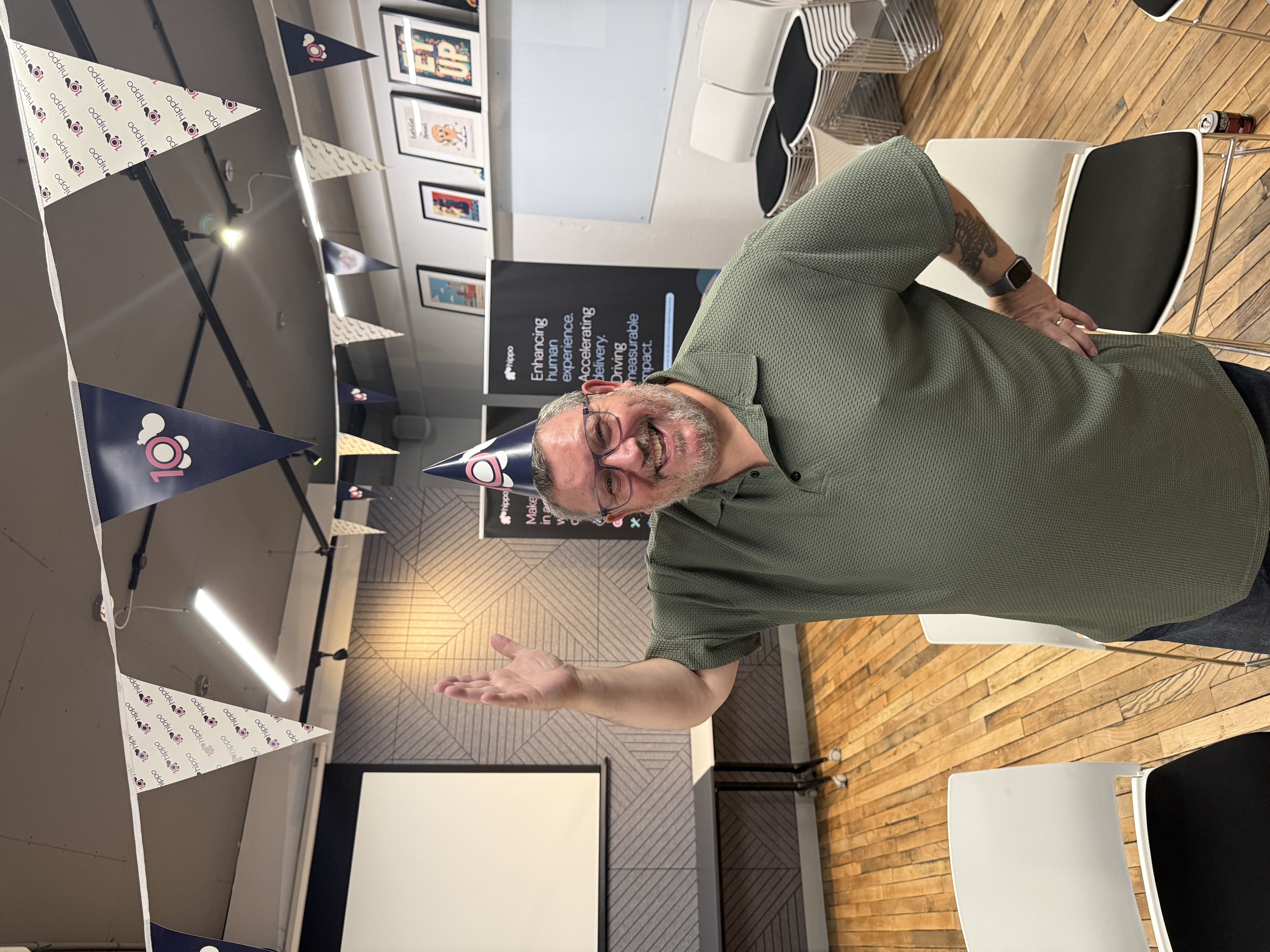 Ady Stokes with a 10 Hippo party hat pointing to a banner with Hippo 10 and logos  image