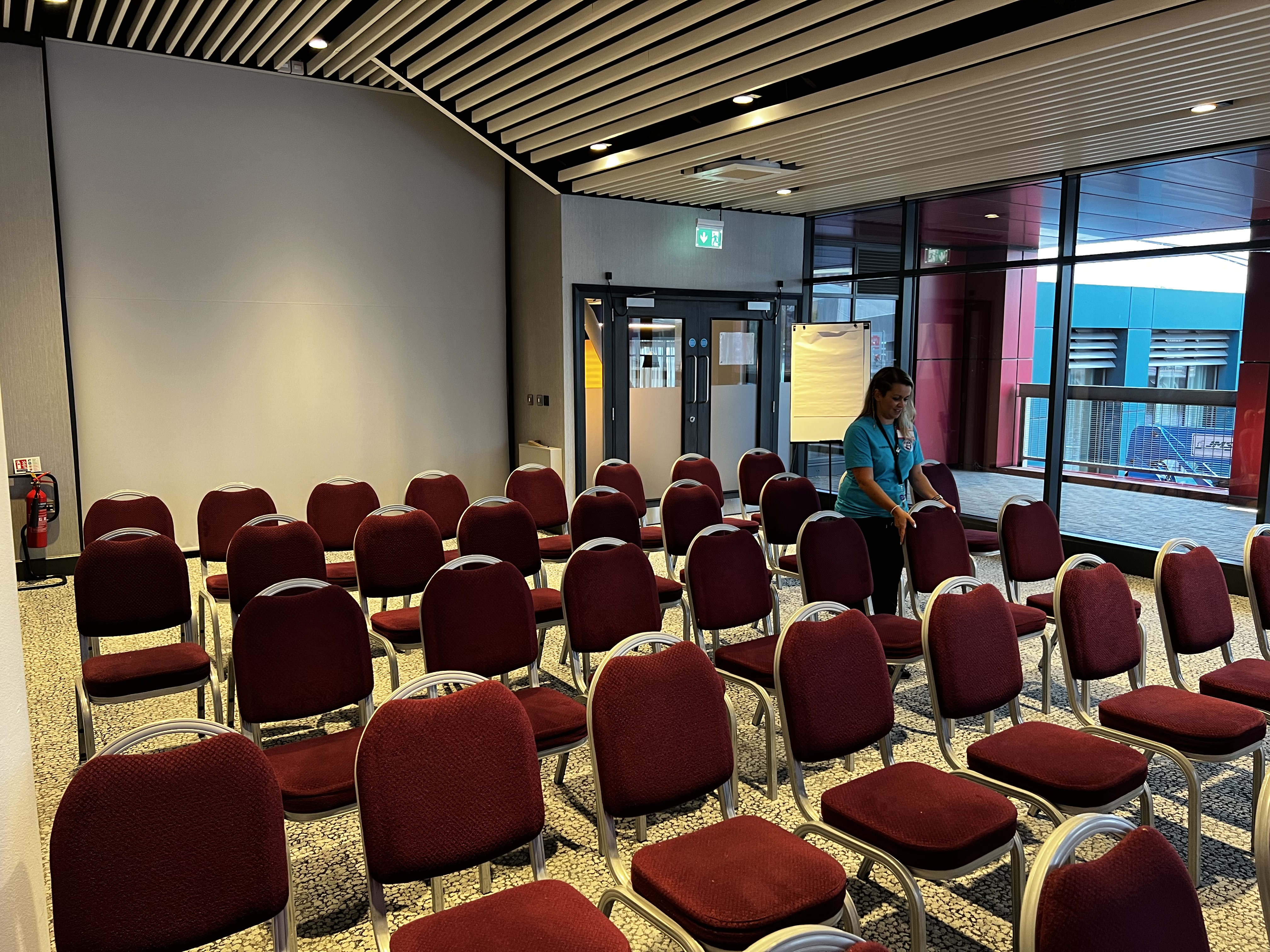 A woman is lining up several rows of chairs. There is concentration and satisfaction on her face. 