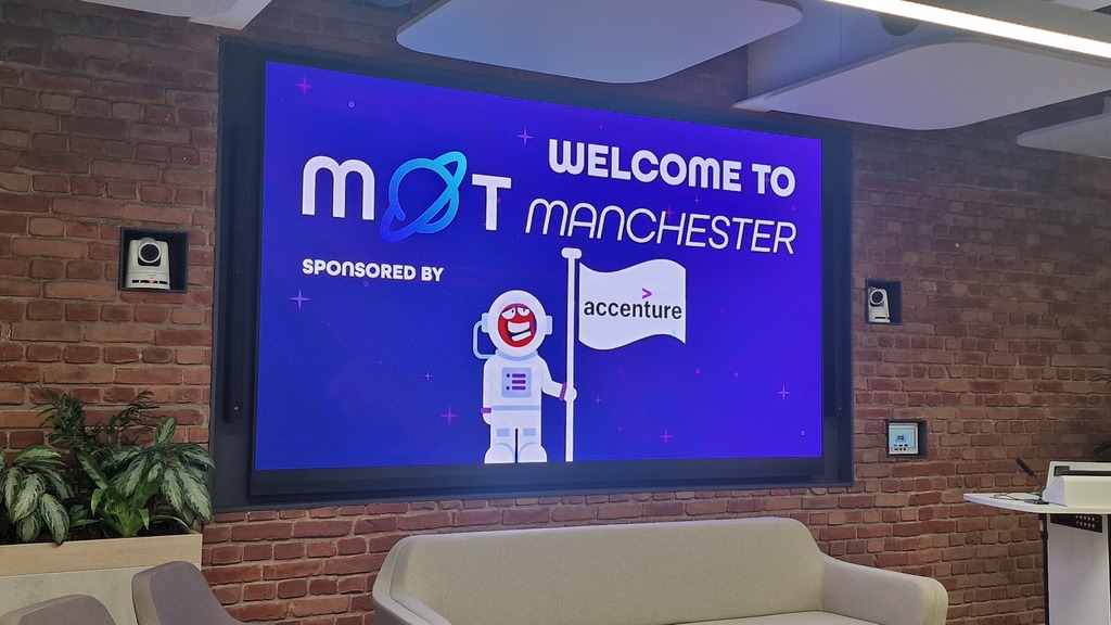 A photo of a large digital screen mounted on a brick wall in a modern office space. The screen displays a purple, spa... image