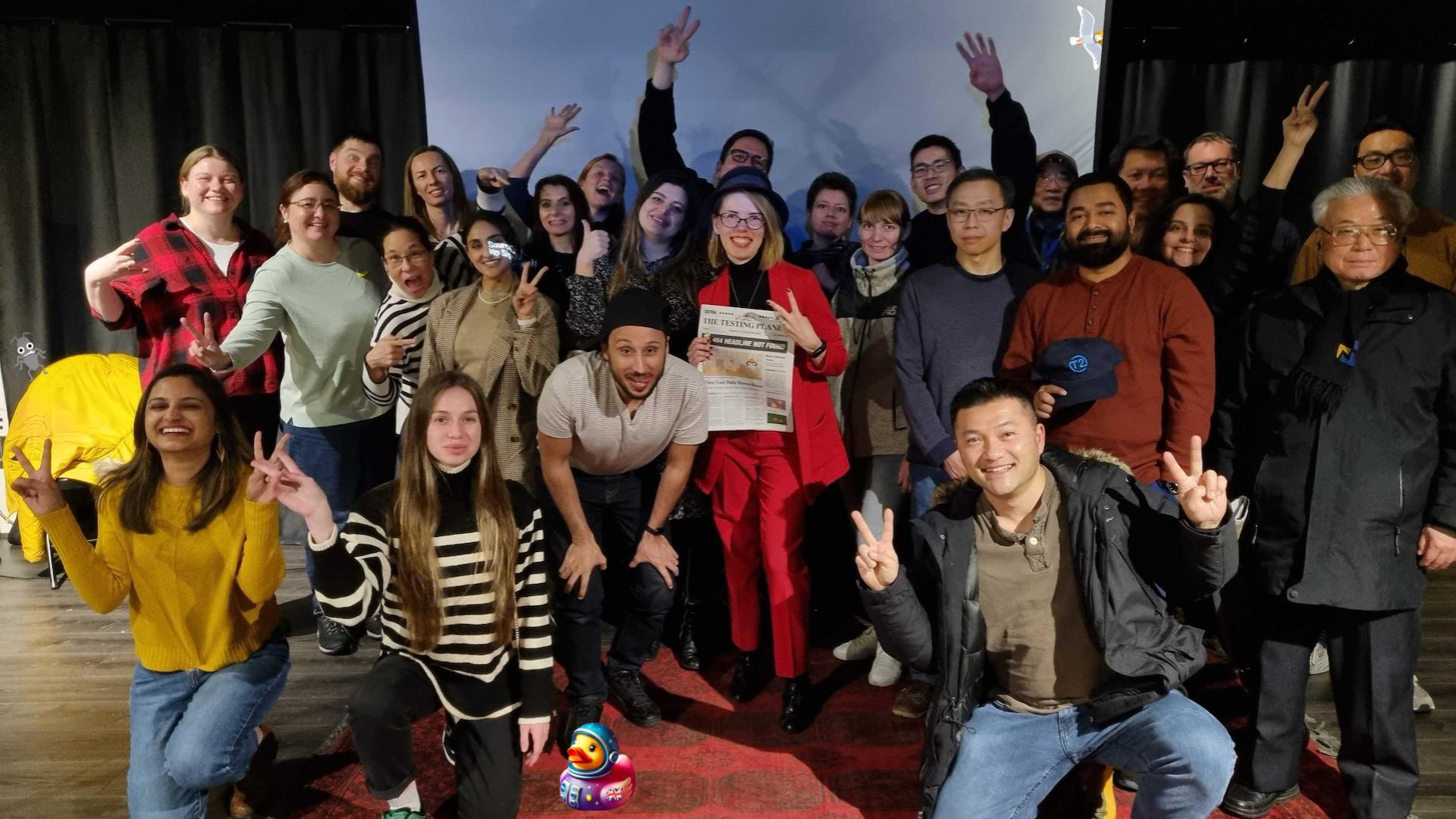 A medium-sized group of people posing for a photo. Most stand and a few kneel. Some have their hands raised in various positive gestures. A duck, seagull and bug character have been added to the image.